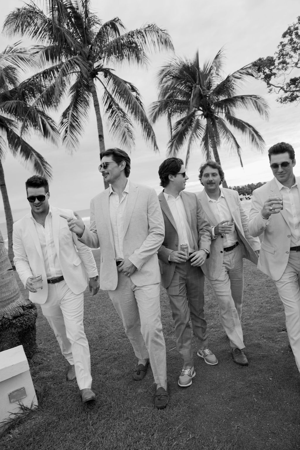 Candid black and white photograph of wedding guests walking beneath palm trees