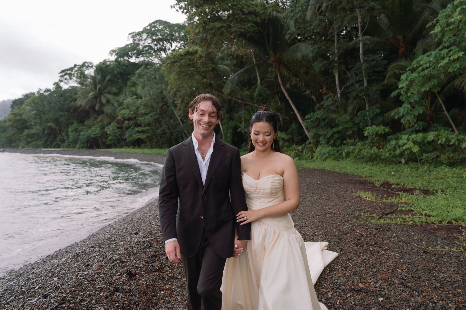 Couple walking together along a tropical beach surrounded by rainforest