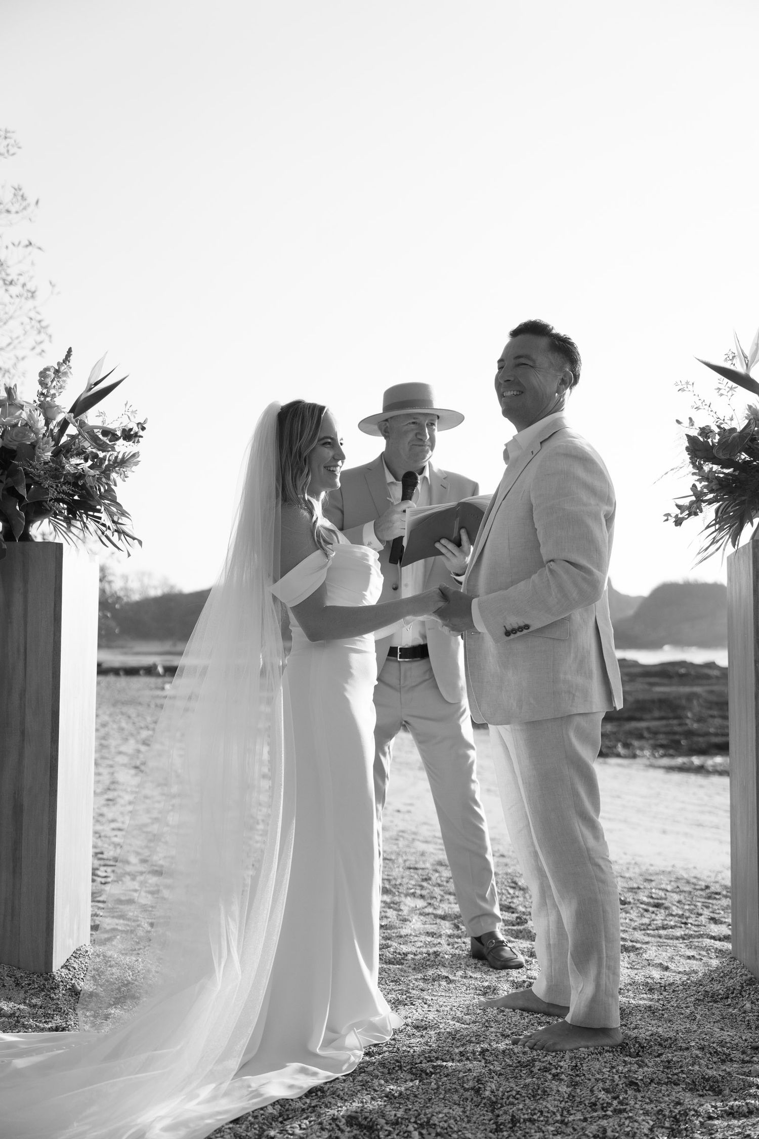 Black and white photo of a bride and groom exchanging vows outdoors with an officiant during a beach wedding ceremony in costa rica