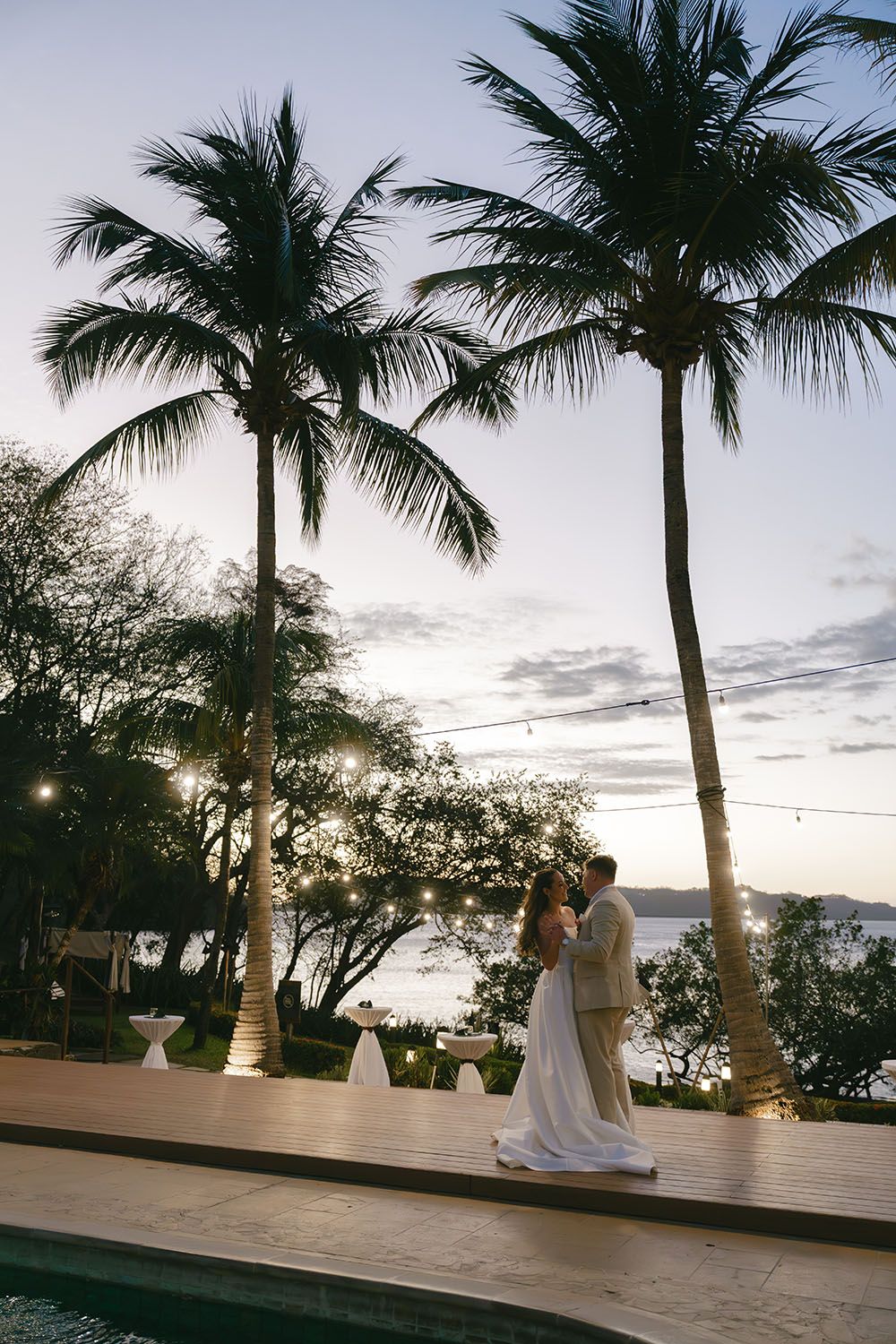 Couple shares romantic first dance at sunset tropical wedding venue with palm trees and string lights by the ocean in costa rica