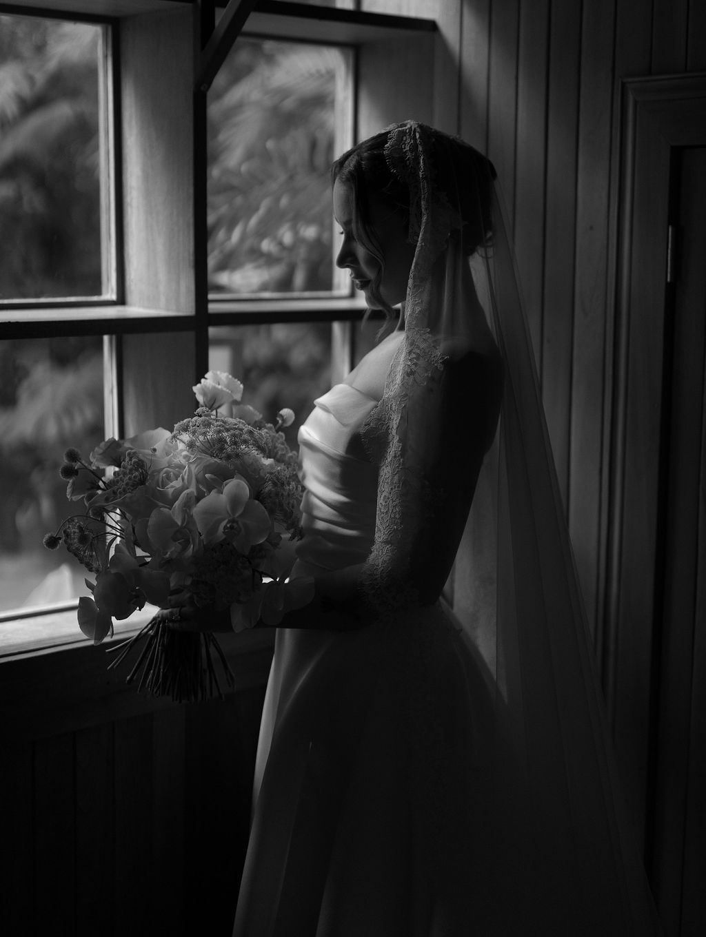 Black and white portrait of a bride holding her bouquet beside a window in Monteverde