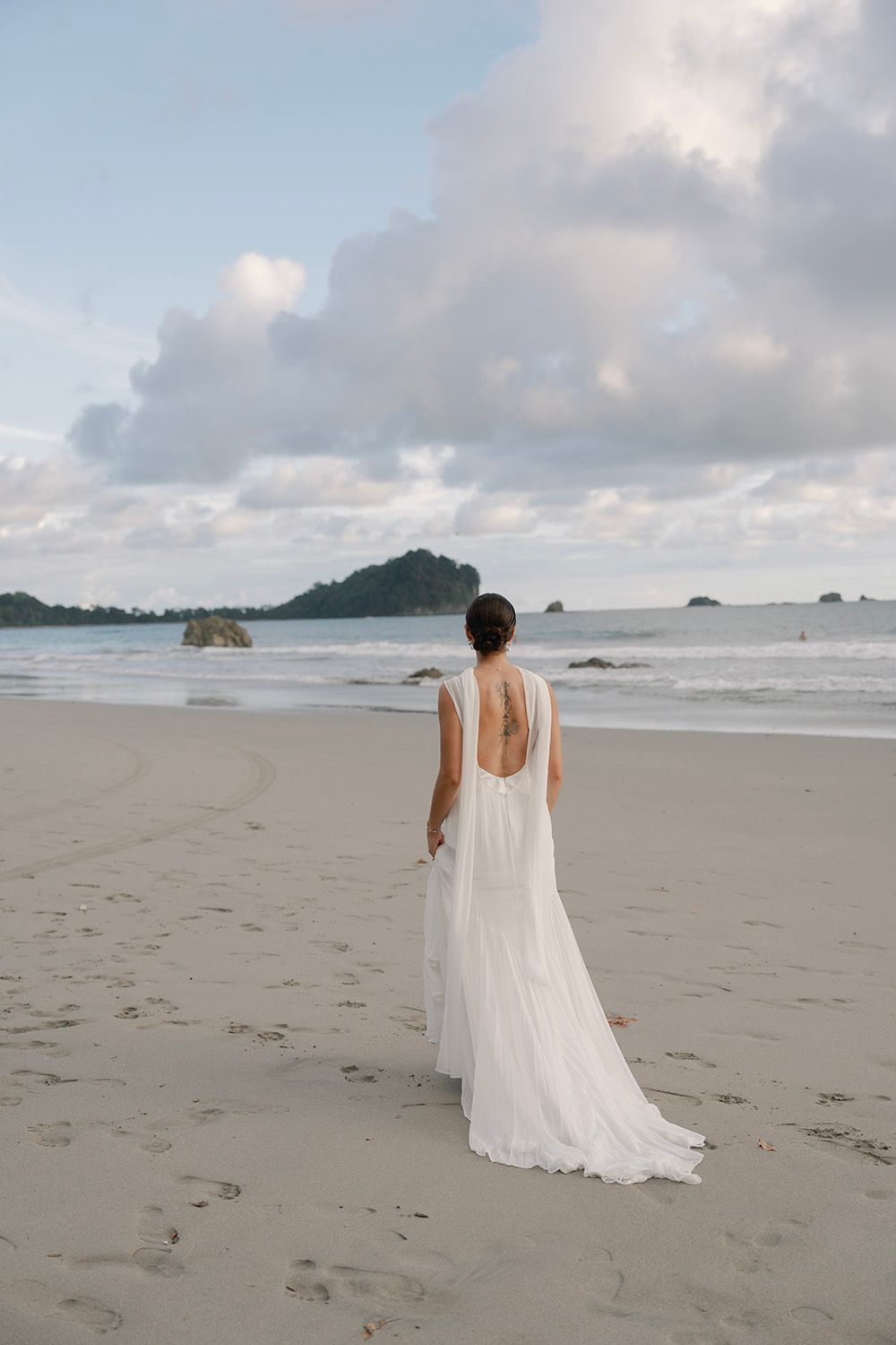 Bride in white backless gown stands on sandy beach gazing in manuel Antonio, costa rica