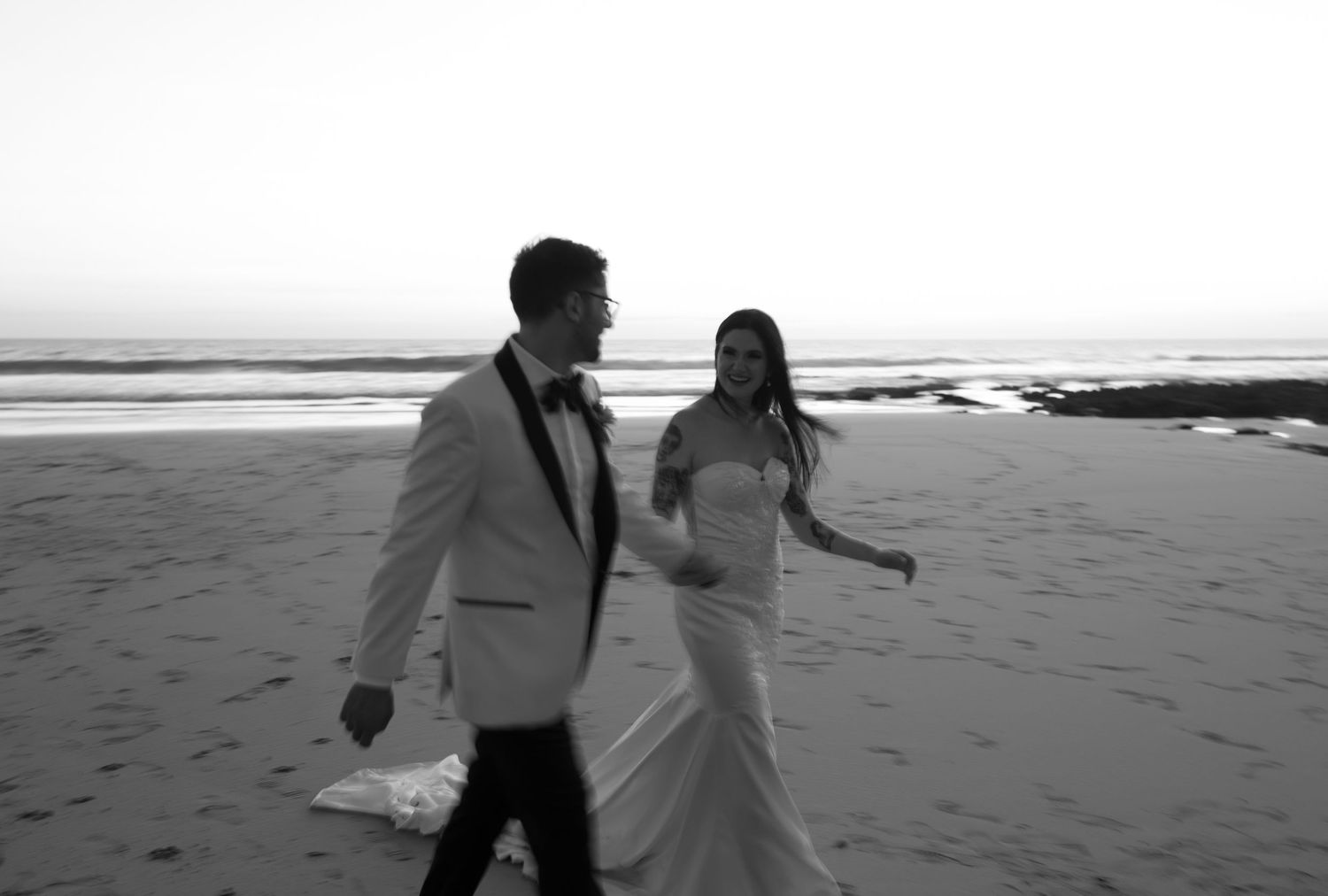 Black and white photograph of newlyweds walking together along the beach
