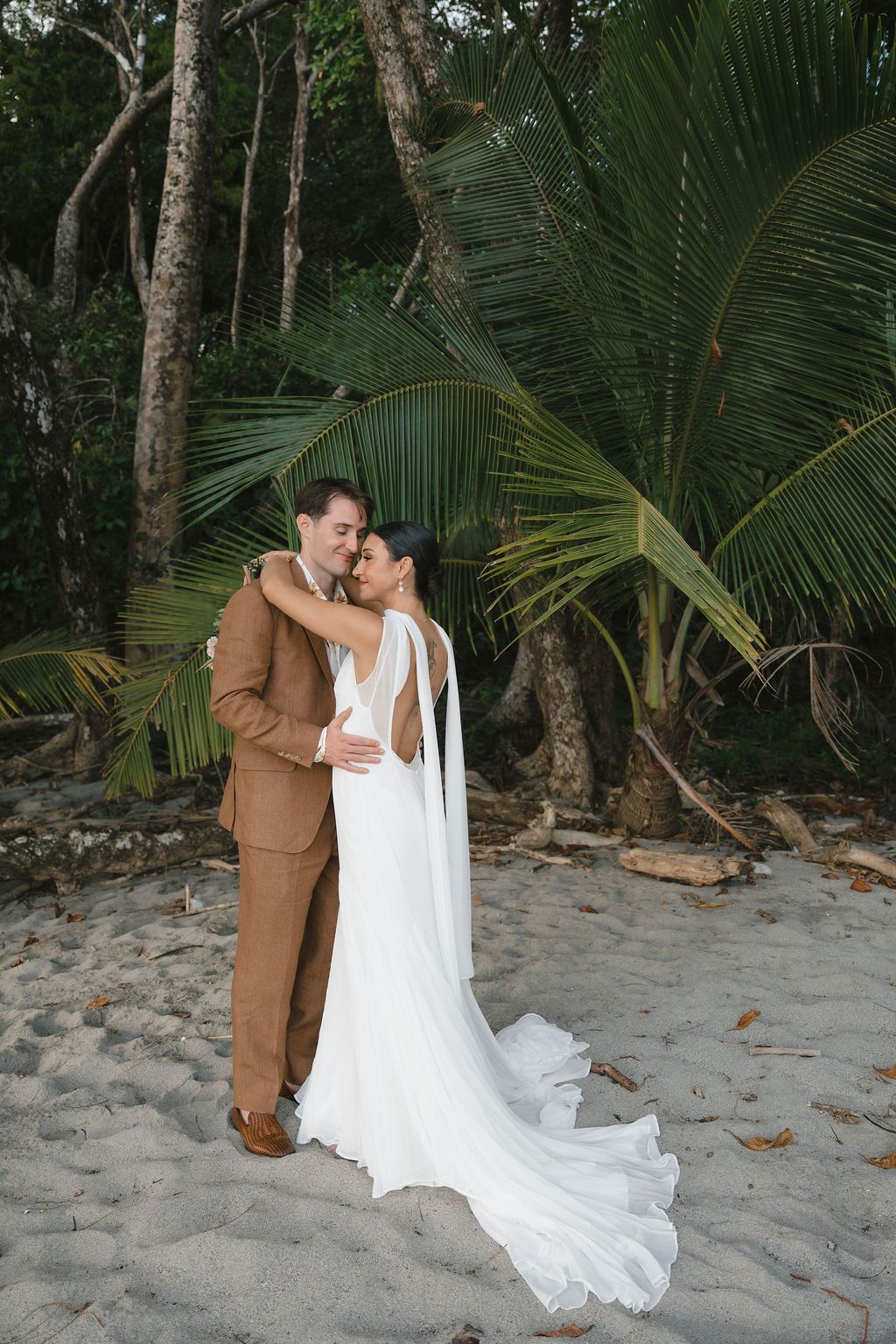 Newlyweds embracing beneath tropical palm trees on a beach in Manuel Antonio.