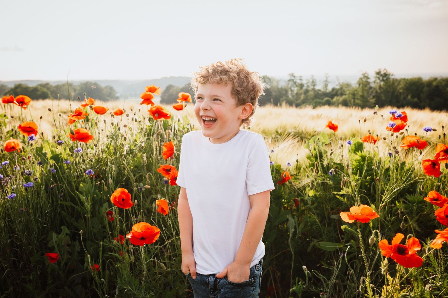 Happy curly-haired boy laughing in a field of bright red poppy flowers.