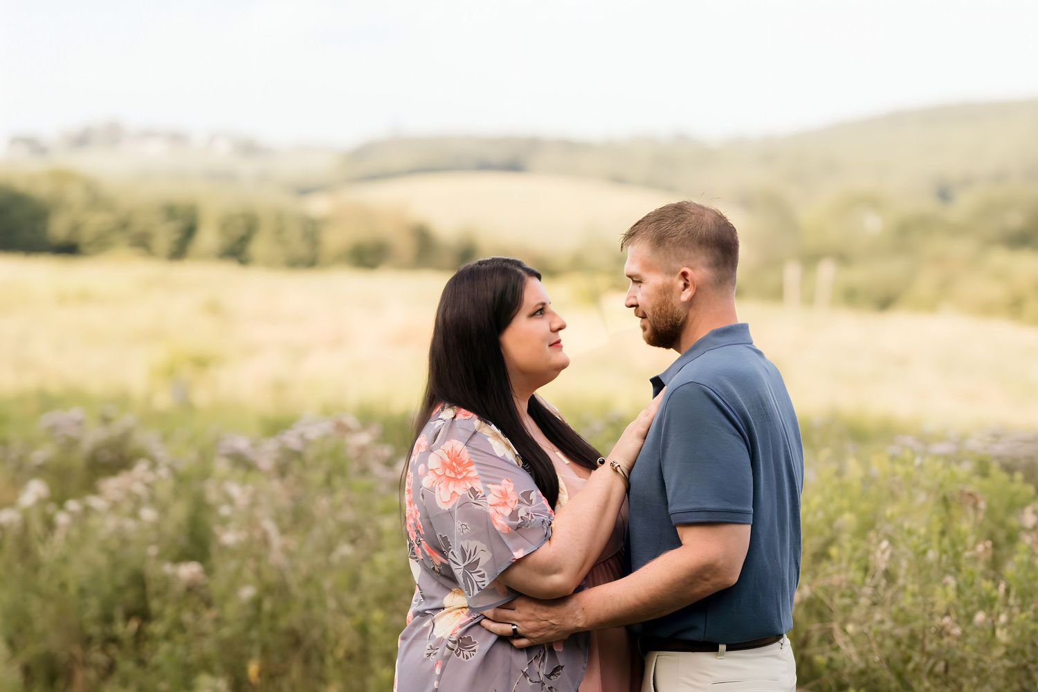 Expecting couple embracing in a golden wildflower field with rolling hills.
