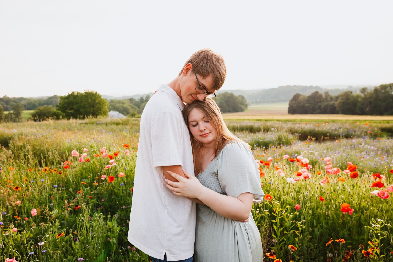 A young couple embraces tenderly in a vibrant poppy field at golden hour.