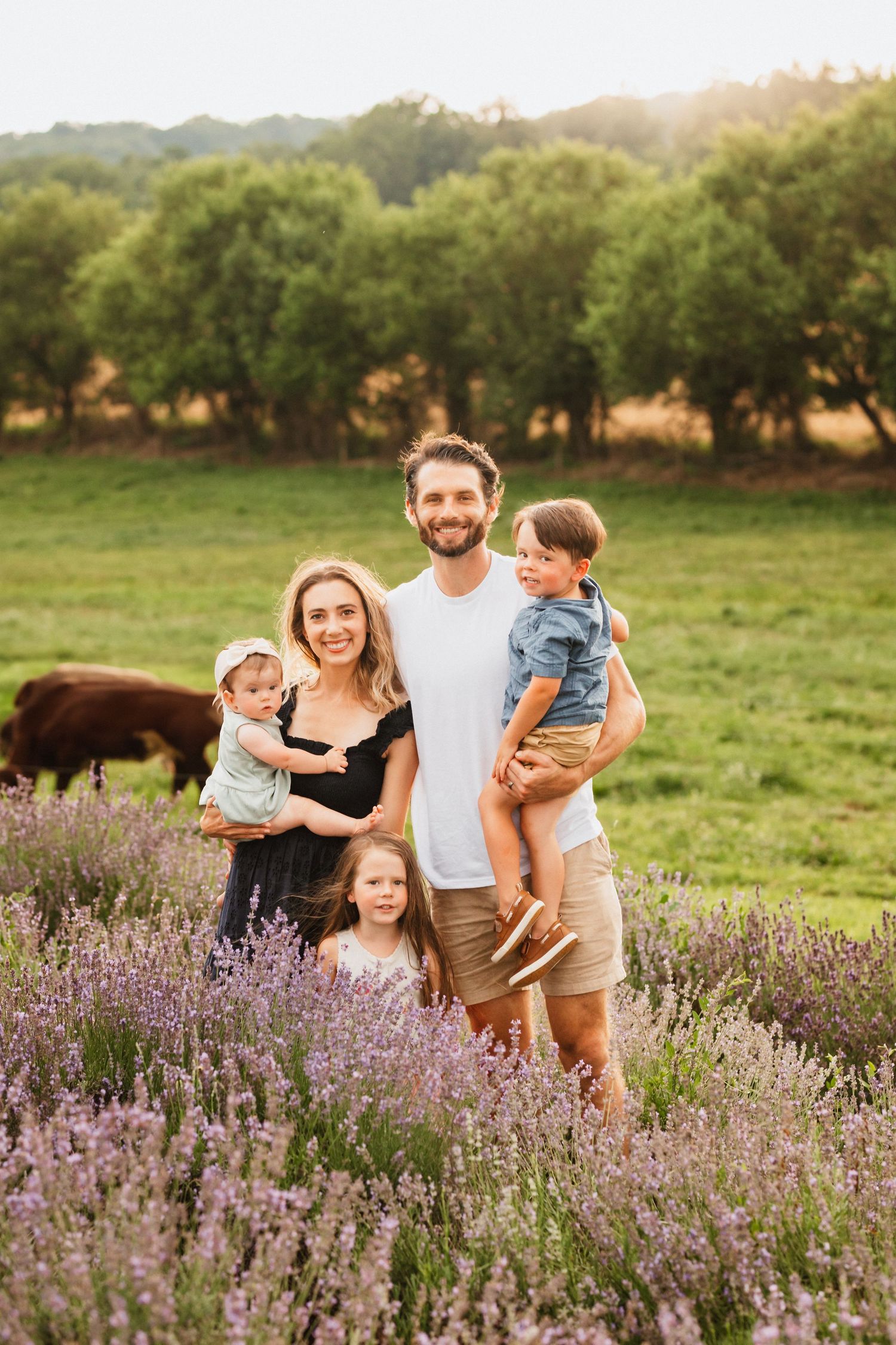 A happy family of five poses in a lavender field with green hills behind them.