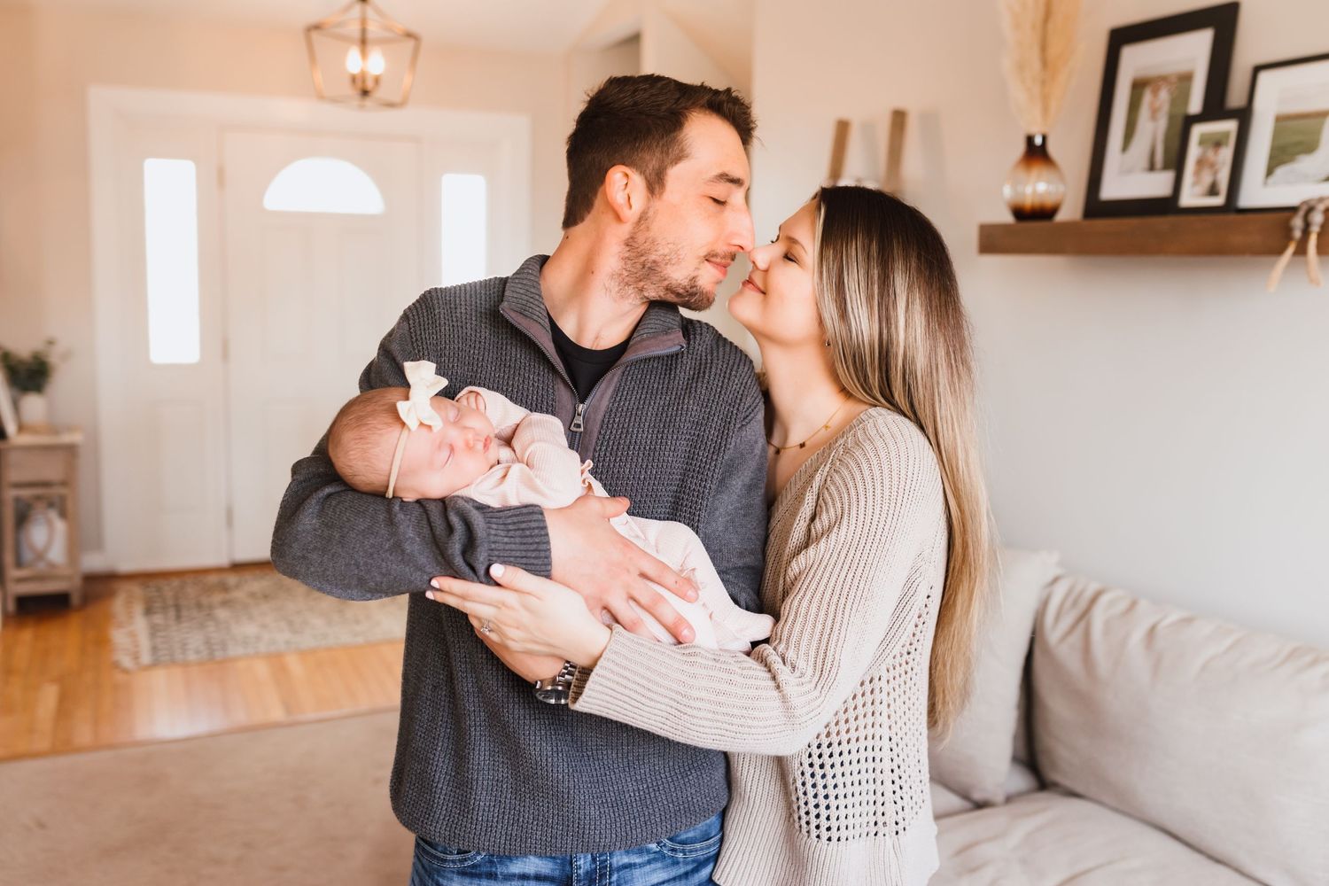 Young couple sharing a kiss while holding their newborn baby in a cozy home.