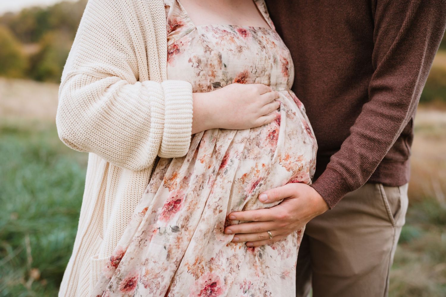 Close-up of a couple's hands cradling a pregnant belly in a floral maternity dress.