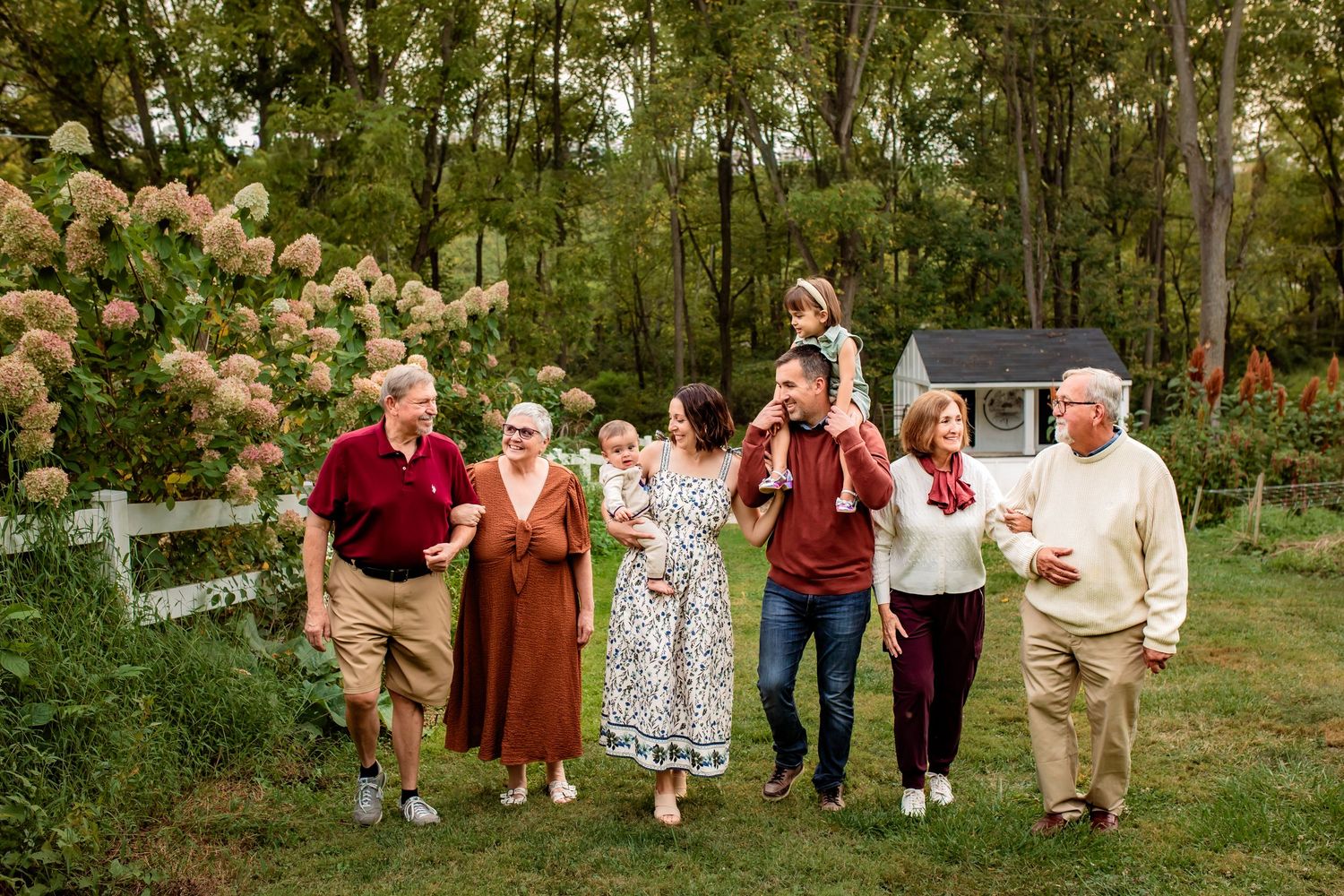 Multi-generational family of seven walking together in a garden with blooming hydrangeas.