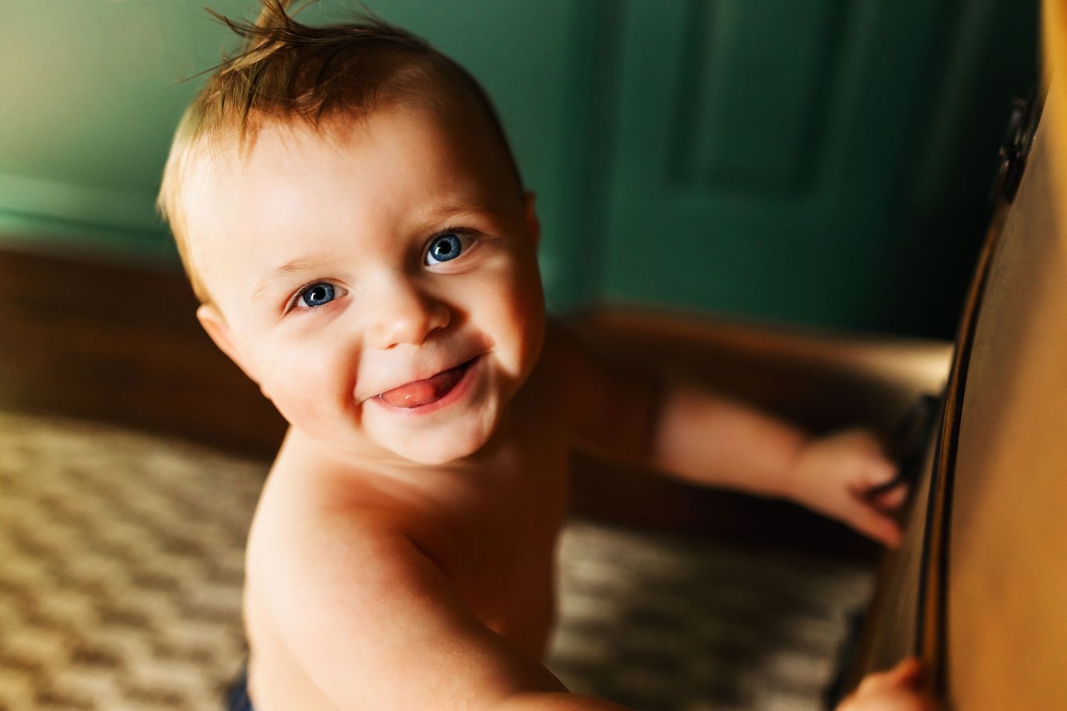 Smiling blue-eyed baby with wet hair looking up in warm indoor lighting.