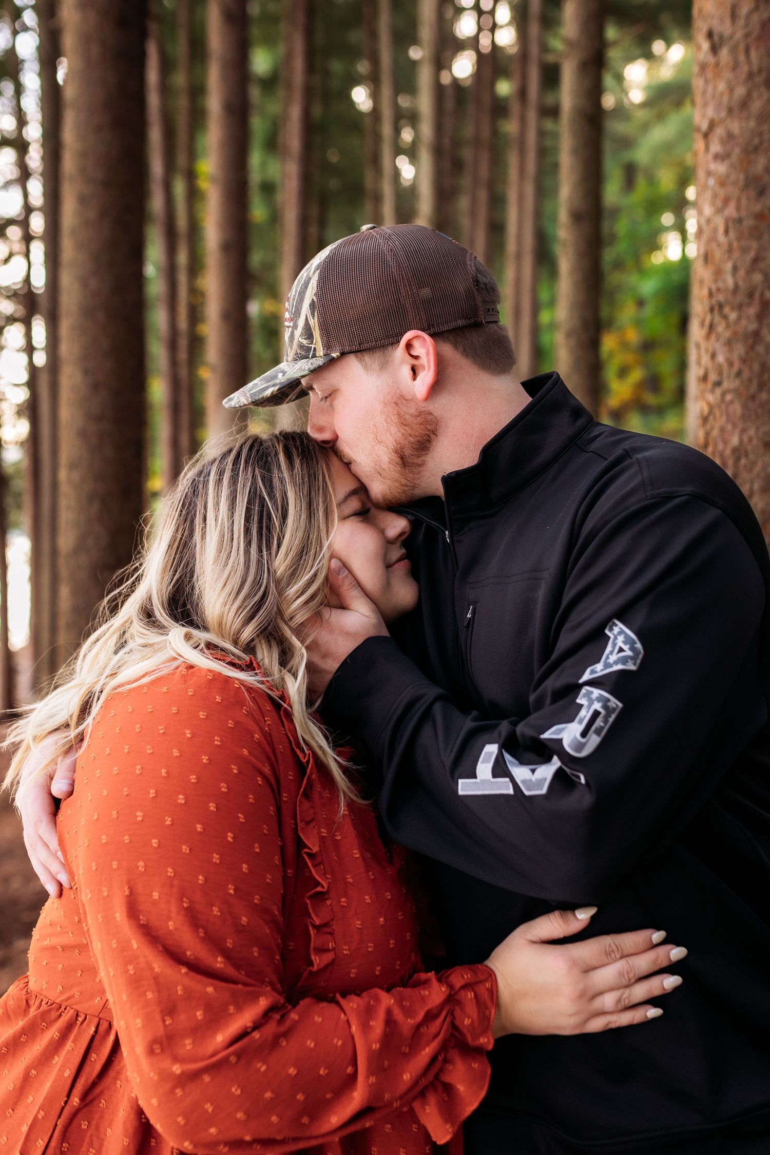 Couple sharing a tender kiss among tall pine trees in a forest.