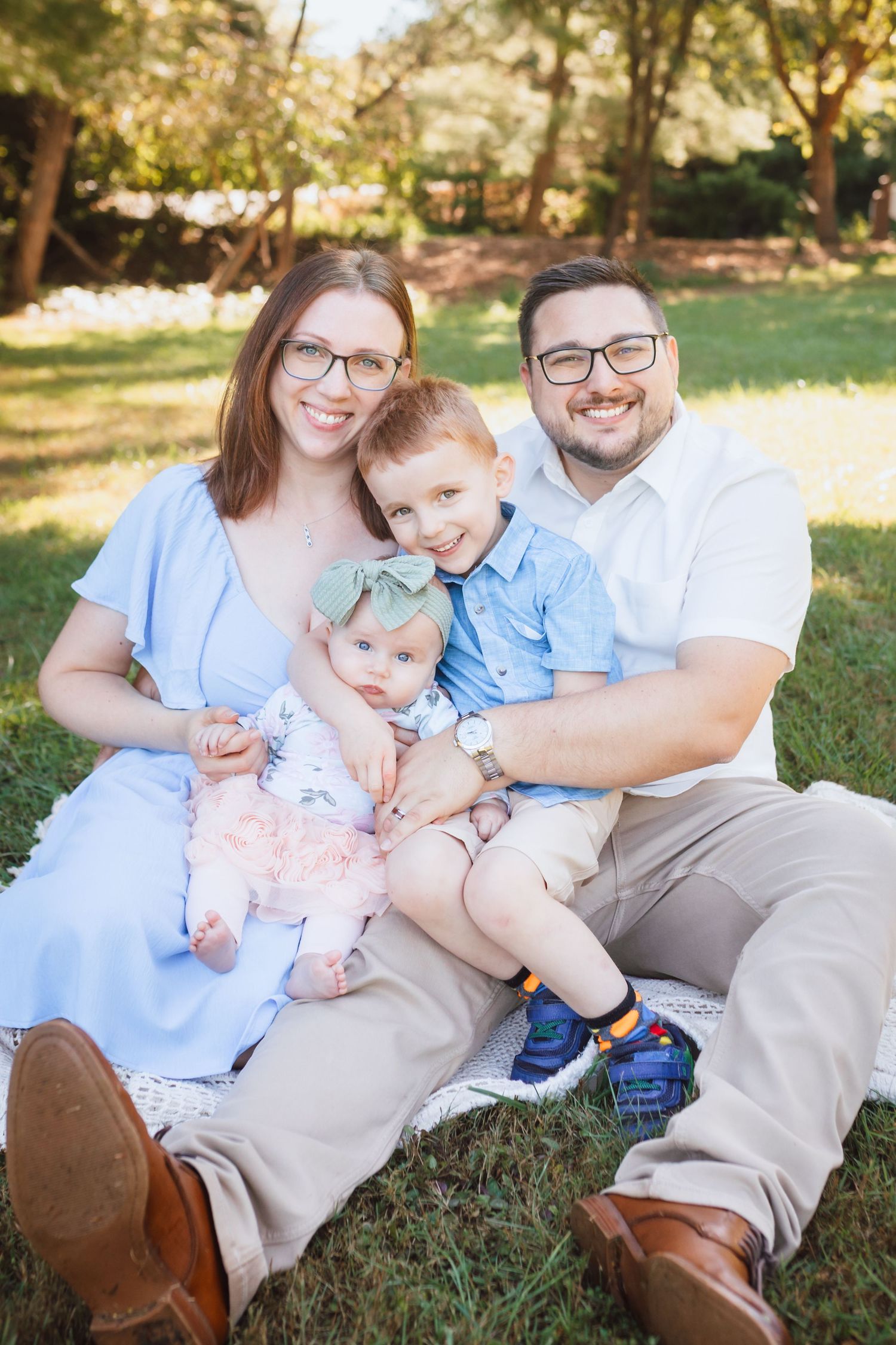 Happy family of four sits together on grass in sunny park setting.