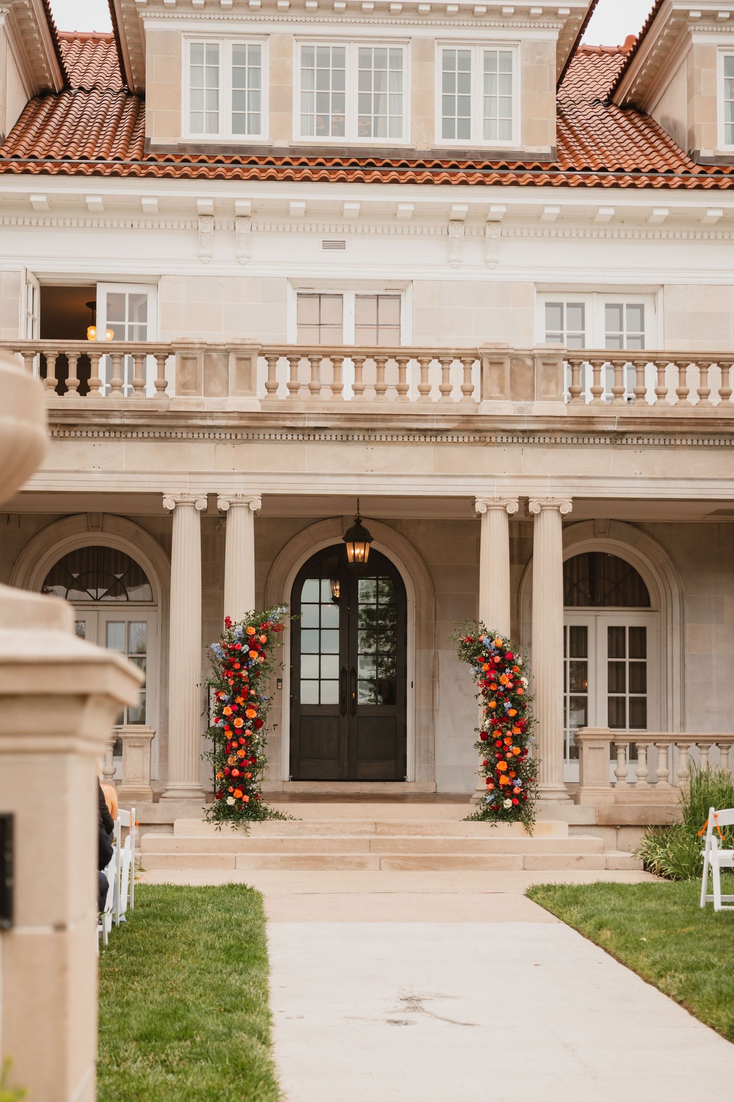 Elegant mansion entrance adorned with vibrant floral arrangements flanking the arched doorway.