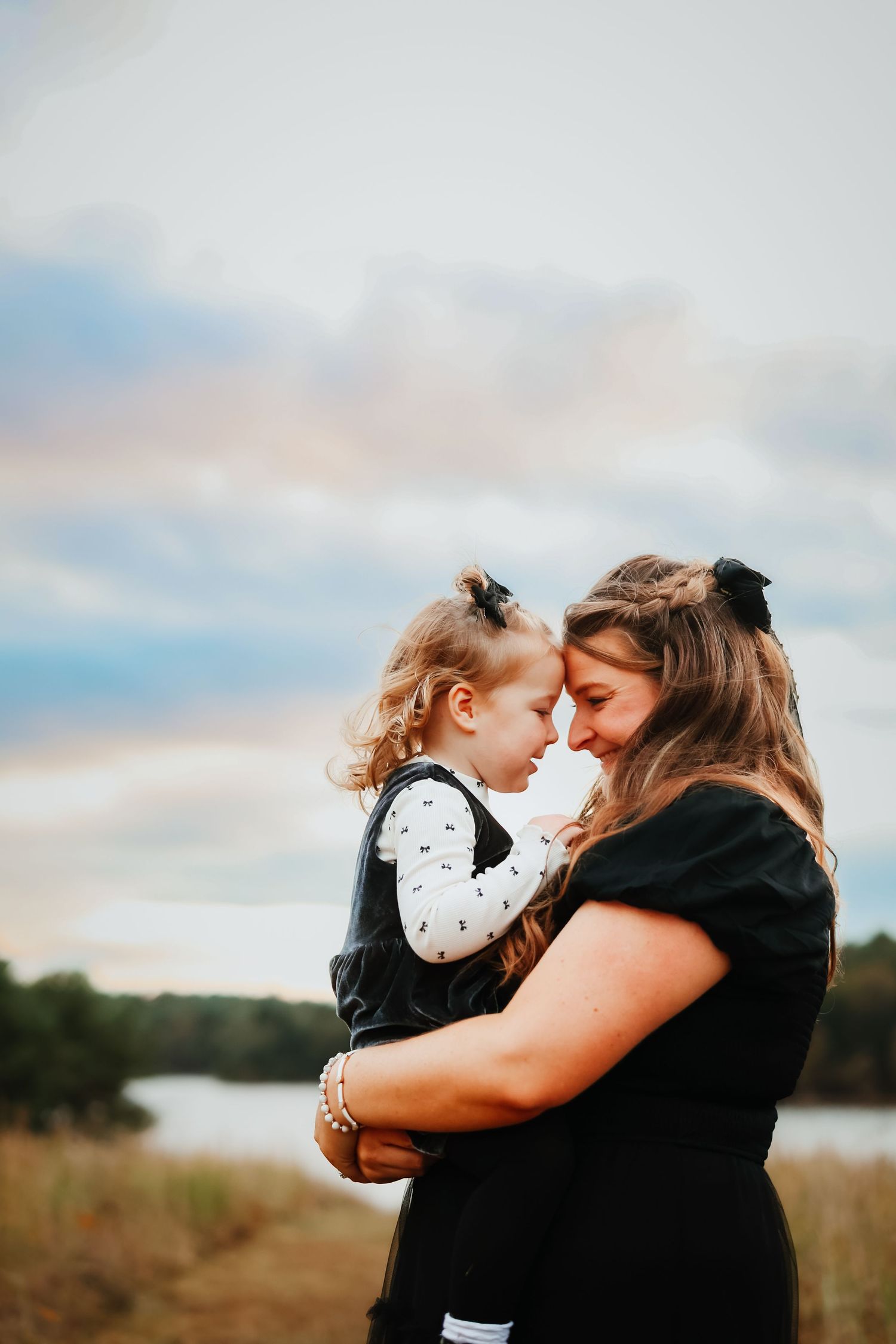 Mother and young daughter touch foreheads in a tender outdoor embrace at sunset.