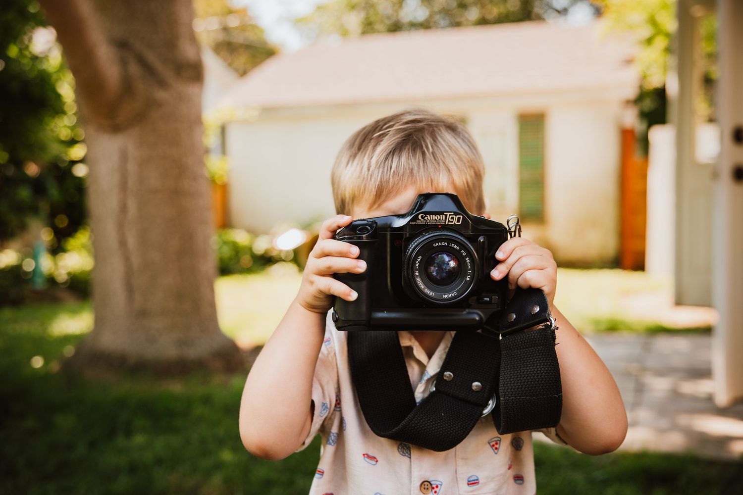 Toddler holding a Canon DSLR camera up to their face outdoors.