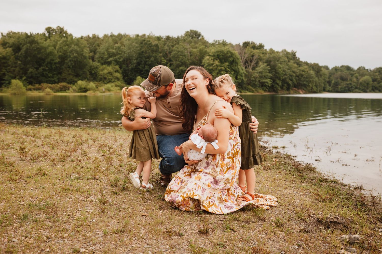 Happy mother with three young daughters sharing hugs by a peaceful lakeside.