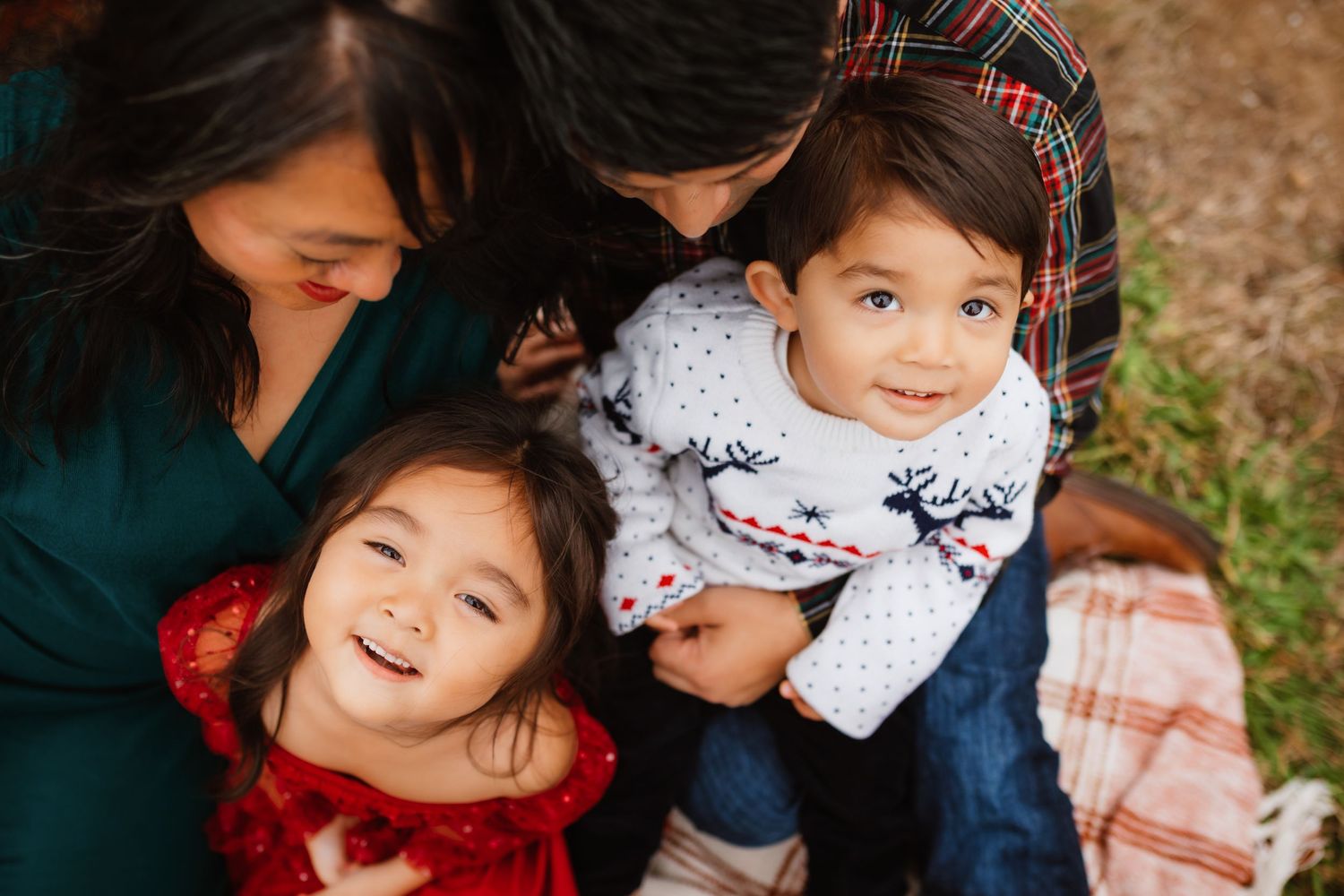 Loving family portrait of parents cuddling two young children outdoors in cozy holiday outfits.