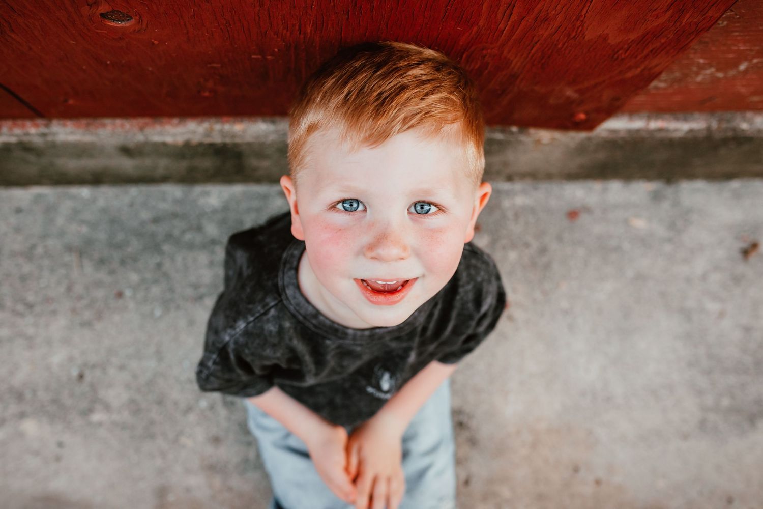 Cheerful red-haired boy in a dark t-shirt smiling up at the camera from below.