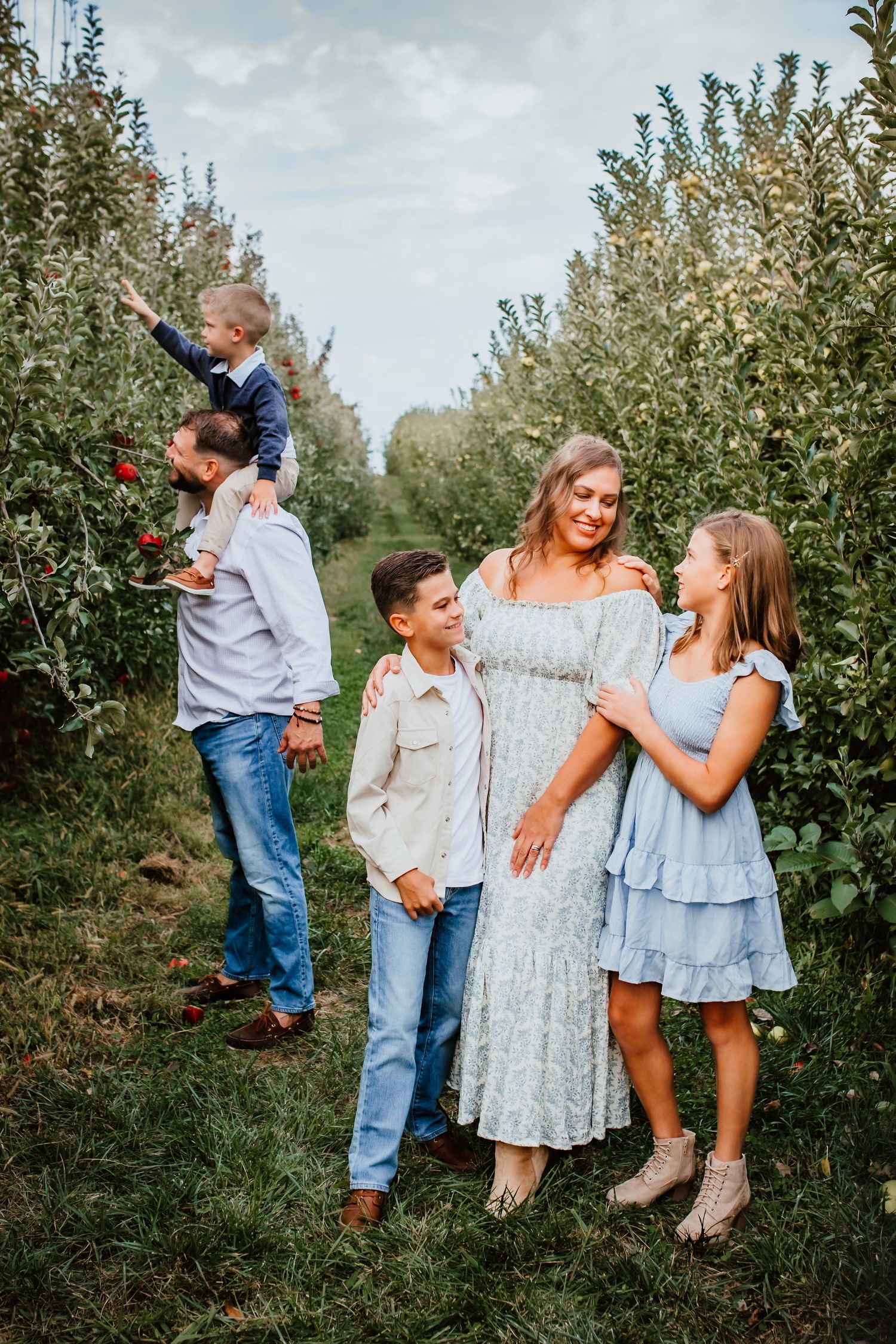 Family of five walking through an apple orchard, dressed in coordinating blue outfits on a cloudy day.