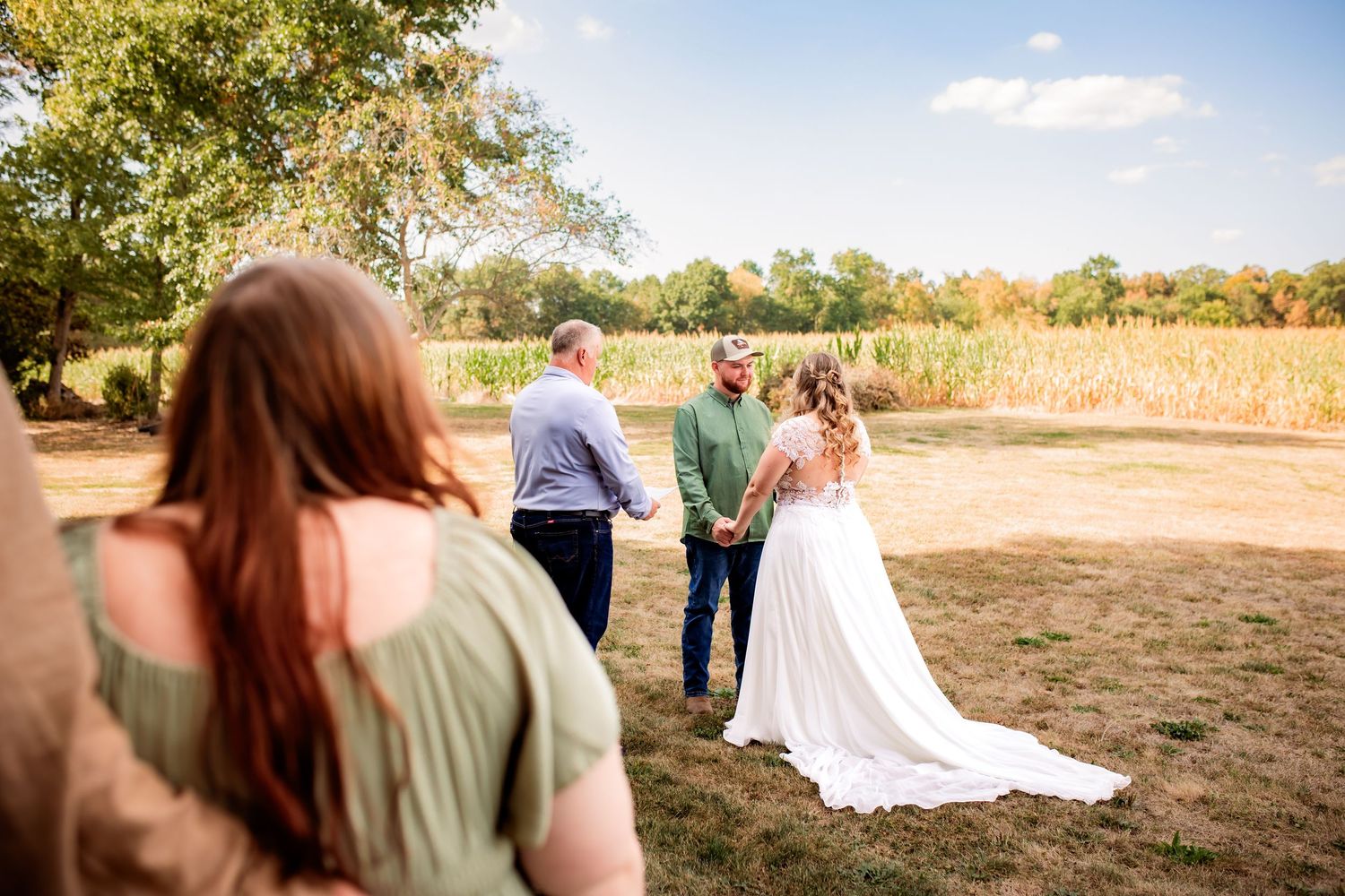 Intimate outdoor wedding ceremony with couple holding hands in golden autumn field.
