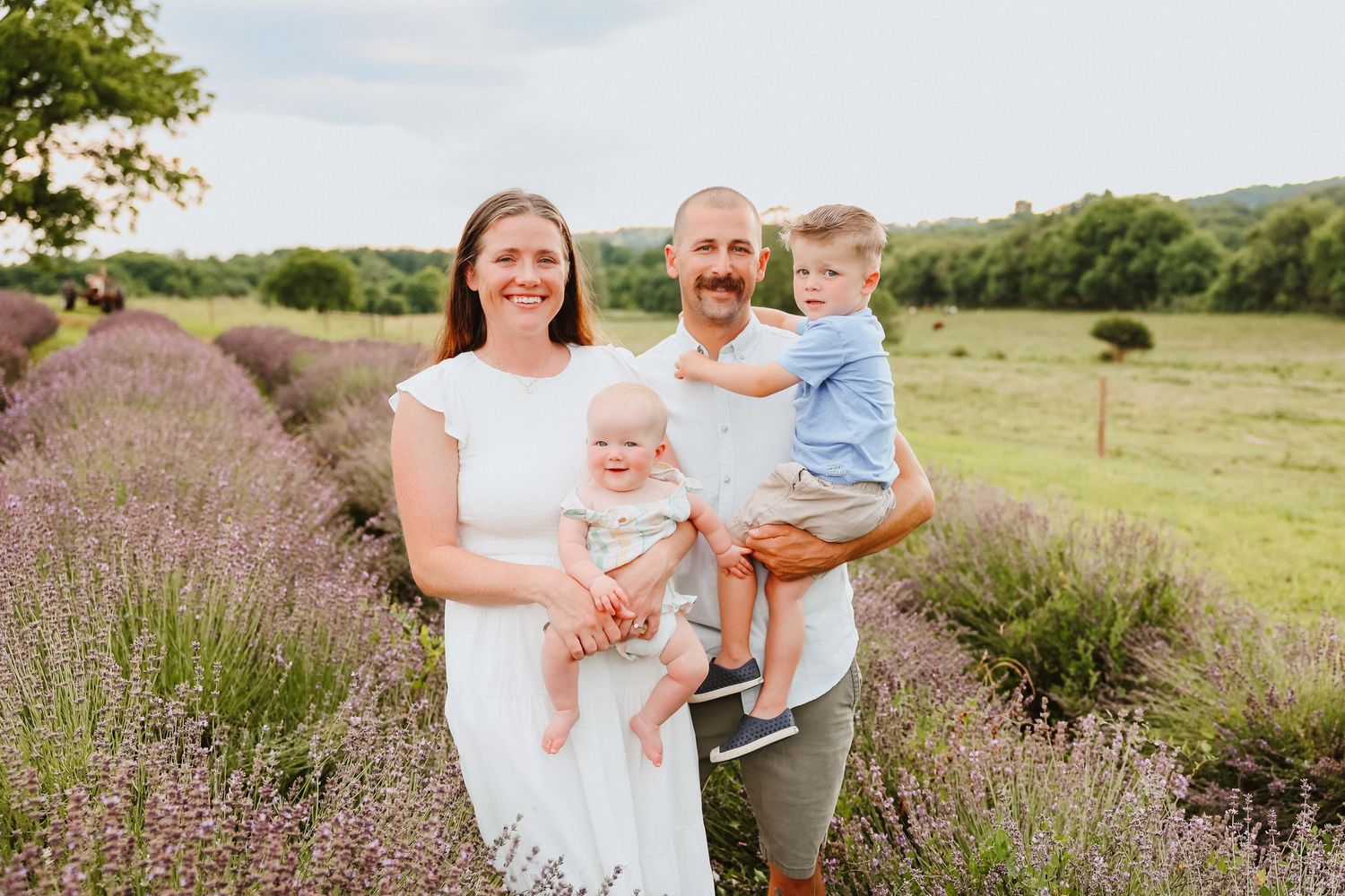 Smiling family of four posing together in purple lavender field.