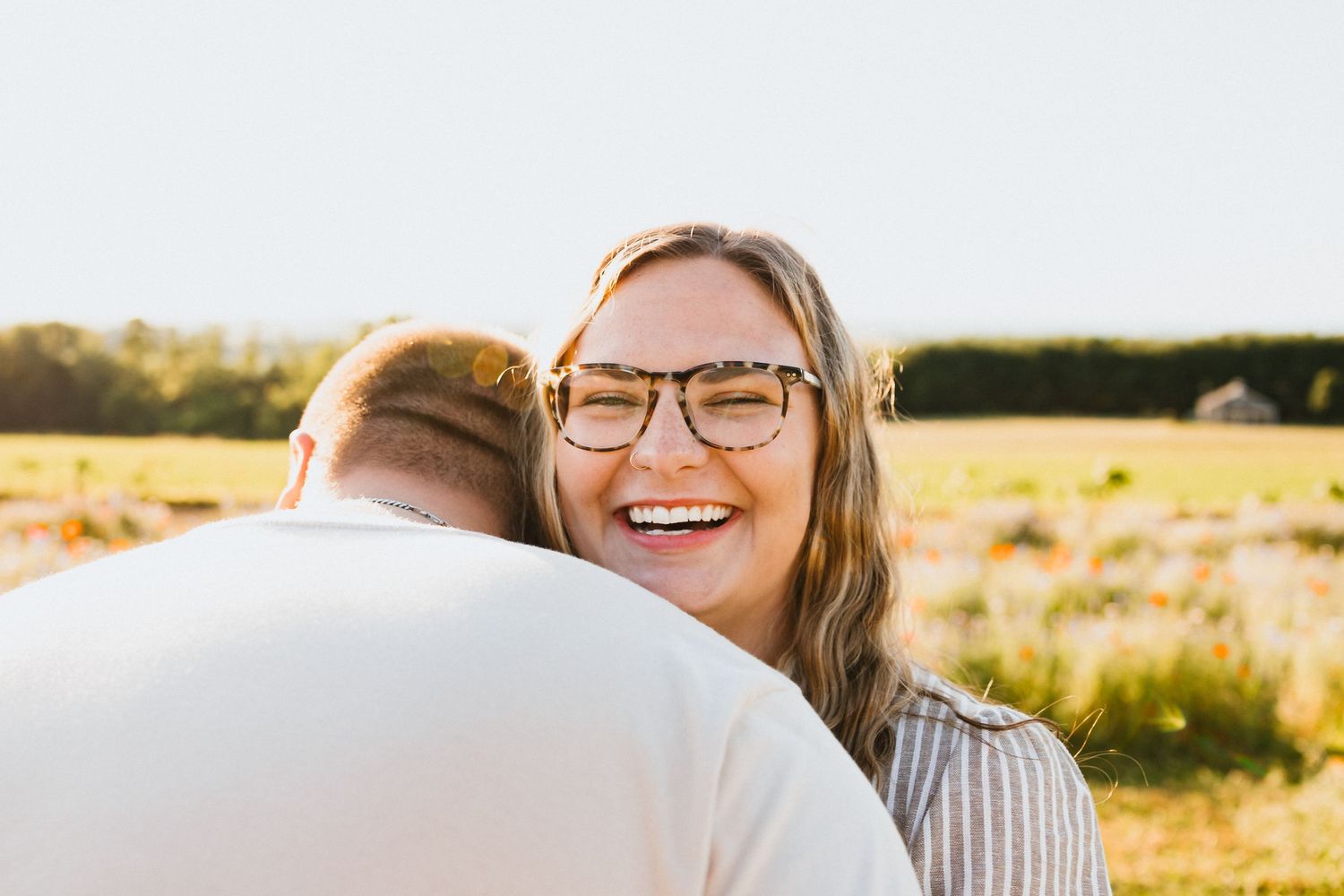 Joyful woman with glasses hugging her partner in a sunny field.