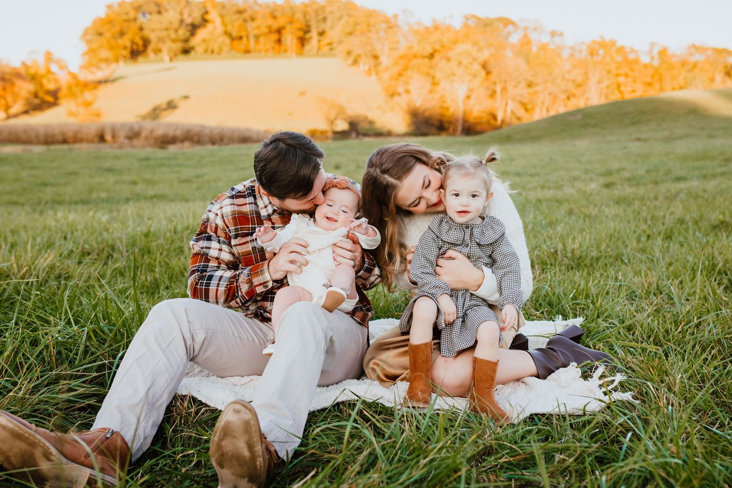 Happy family of four sitting on a blanket in a golden autumn field at sunset.
