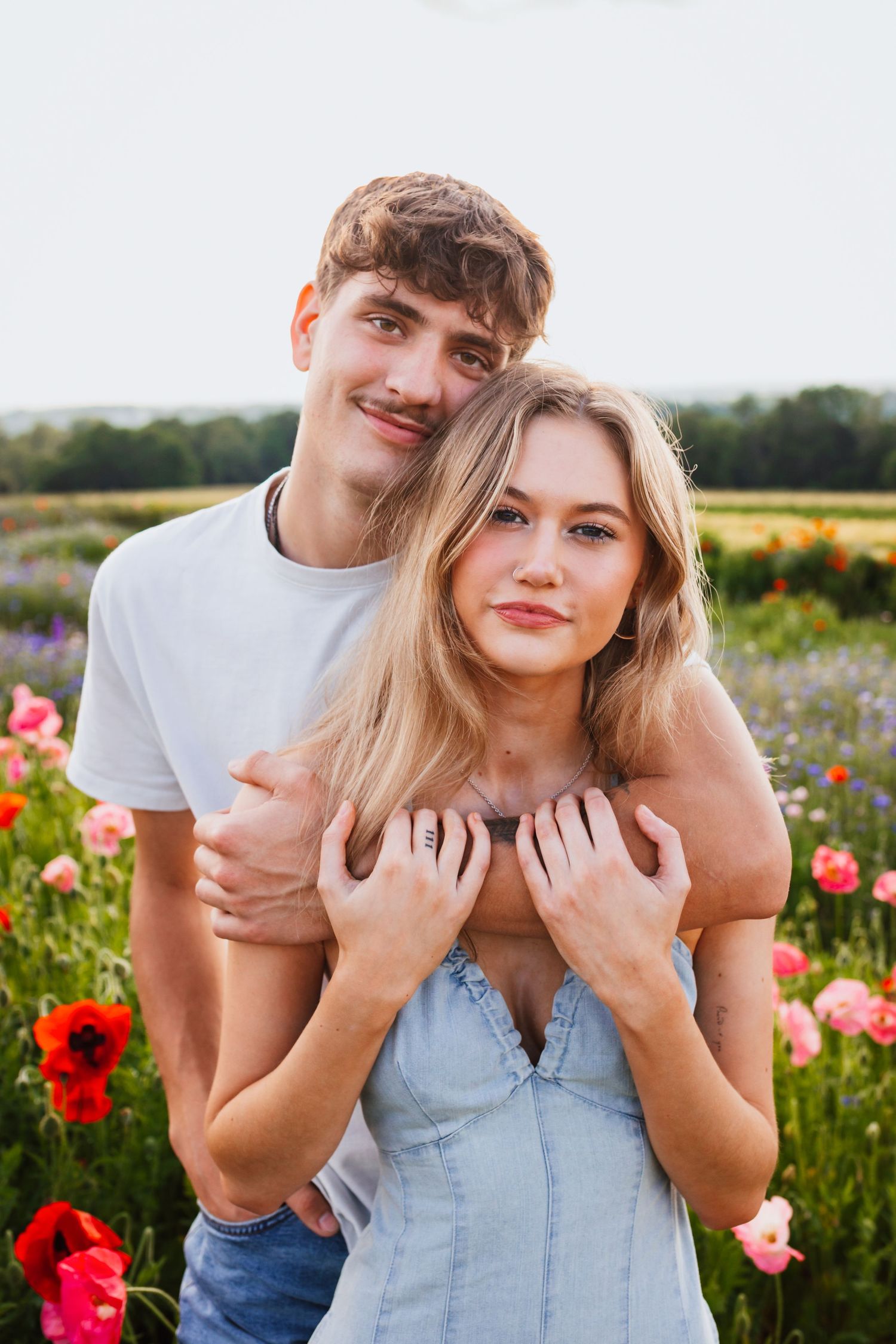 Young couple posing together in colorful poppy field during golden hour.