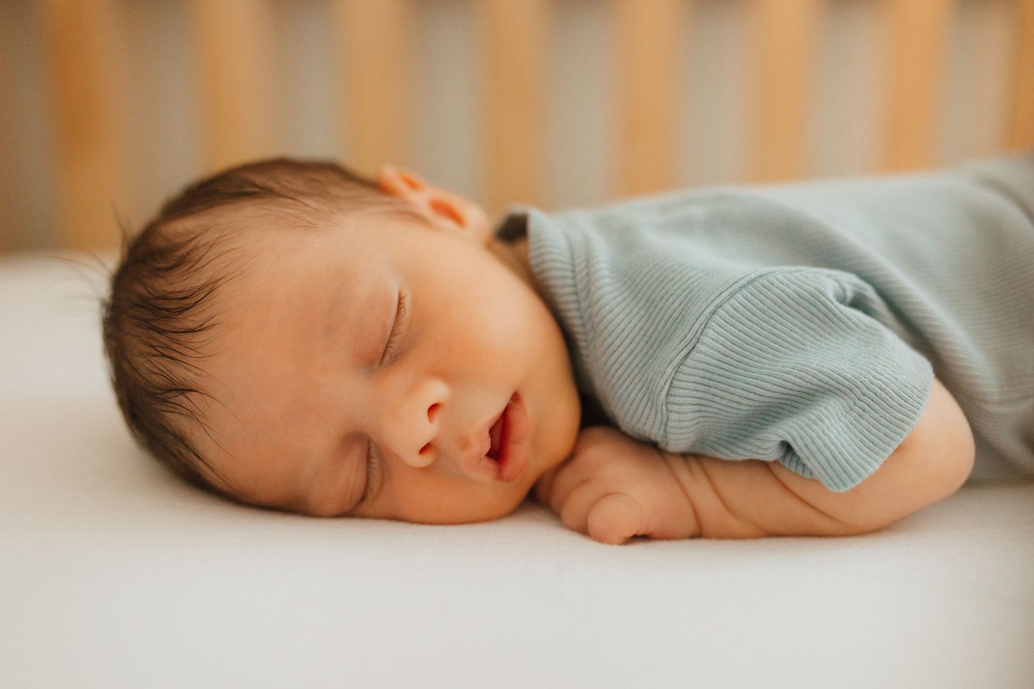 Adorable newborn baby sleeping peacefully in a crib wearing a light blue outfit.