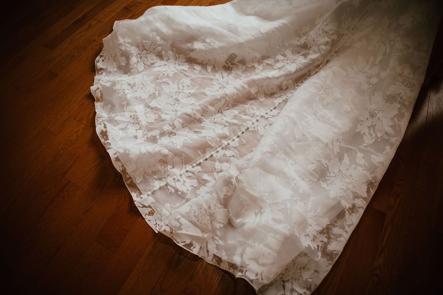 Close-up of intricate lace wedding dress train spread on hardwood floor.
