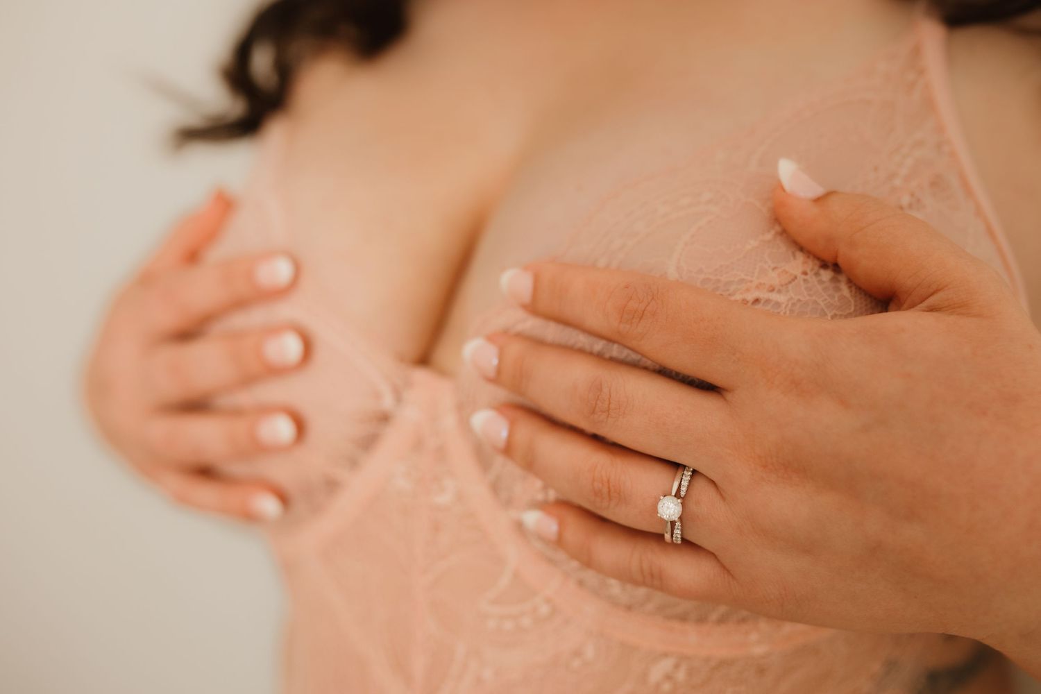 Close-up of woman in pink lace bra with diamond engagement ring on hand.
