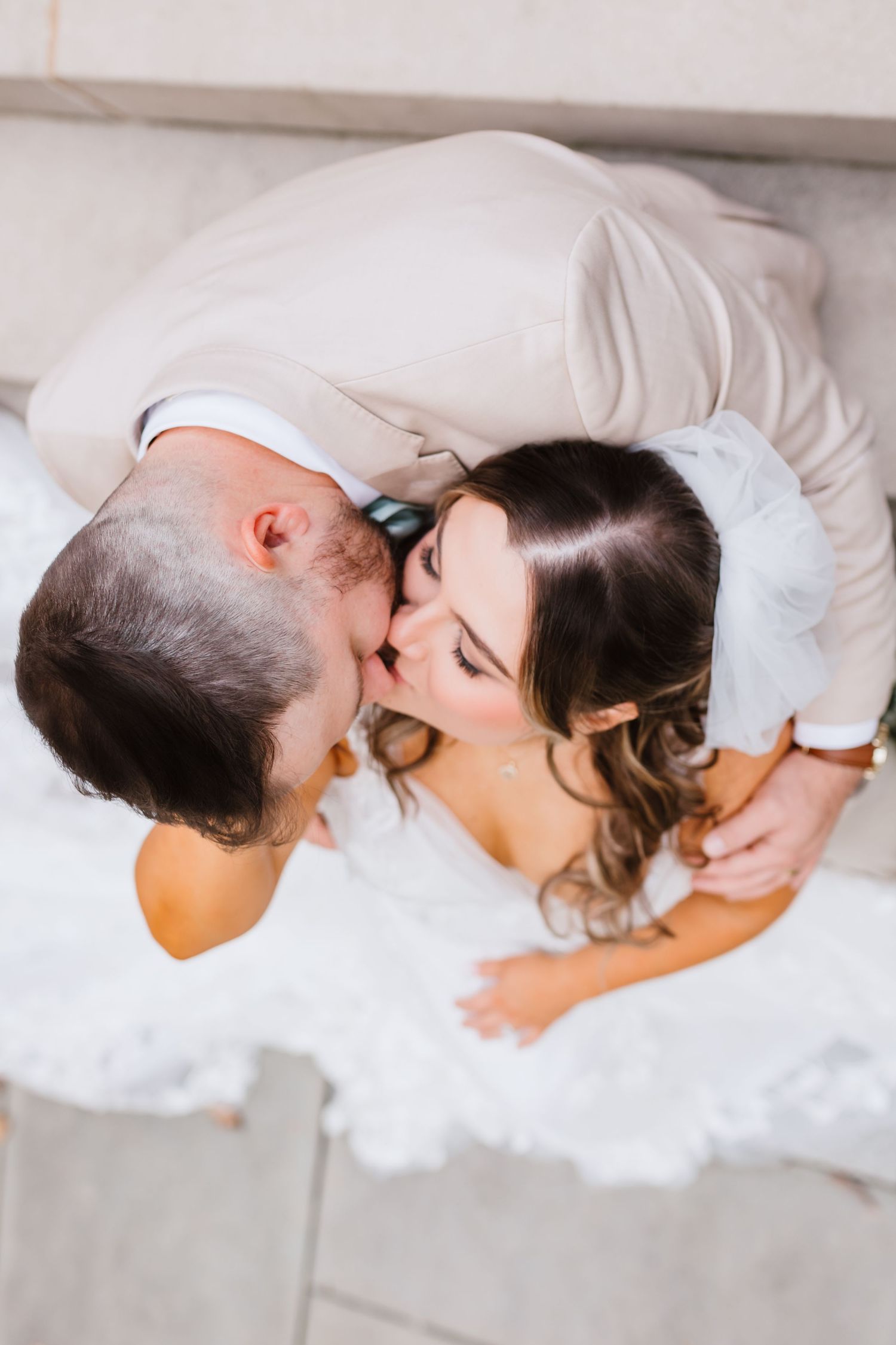 Aerial view of bride and groom sharing a tender kiss while seated on stone steps at their wedding.