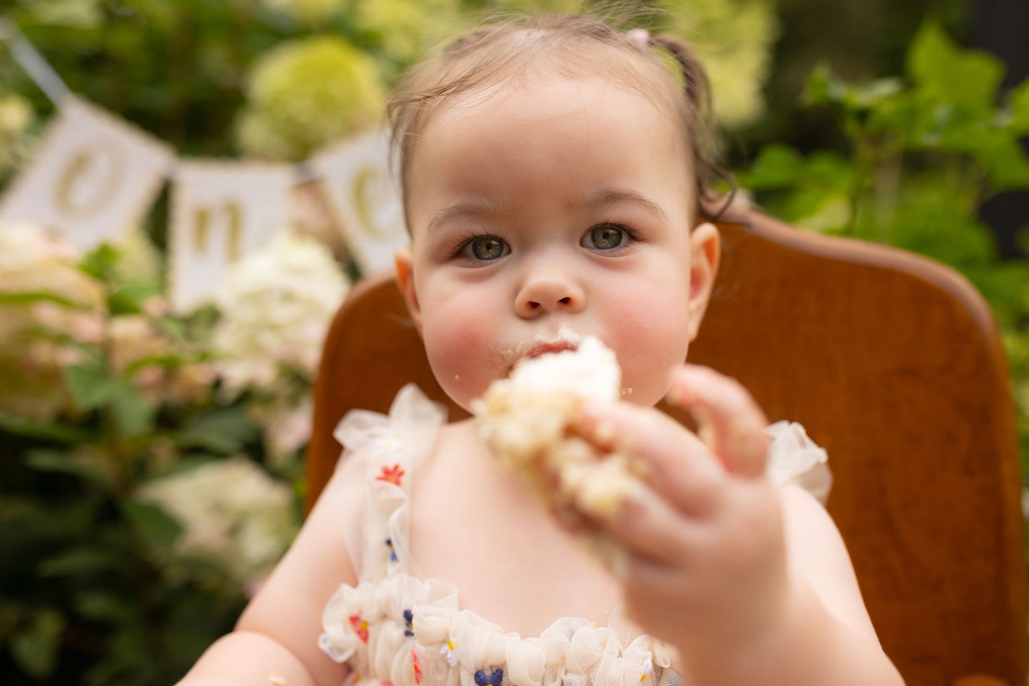 Adorable baby eating birthday cake with frosting on face outdoors.