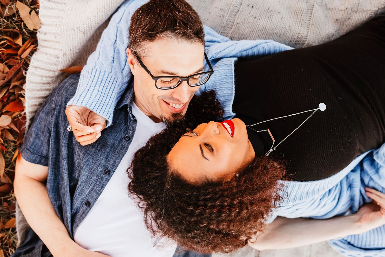Happy interracial couple lying in autumn leaves, smiling and looking at each other.