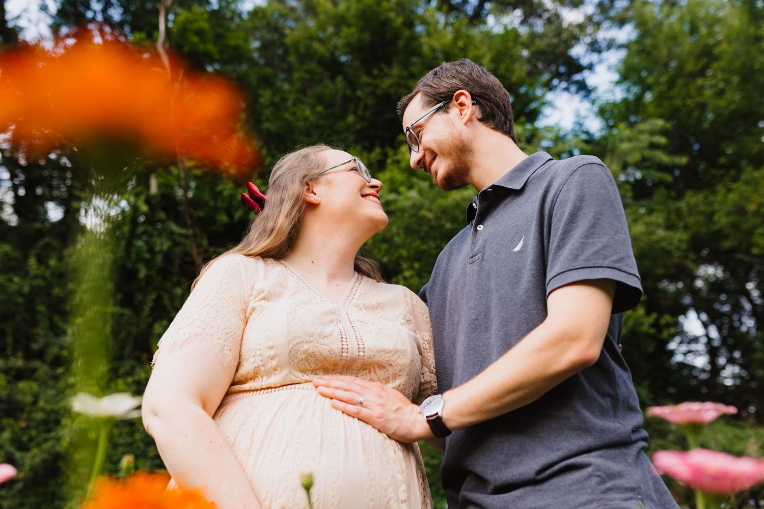 Expecting couple smiling at each other in a colorful flower garden during maternity session.