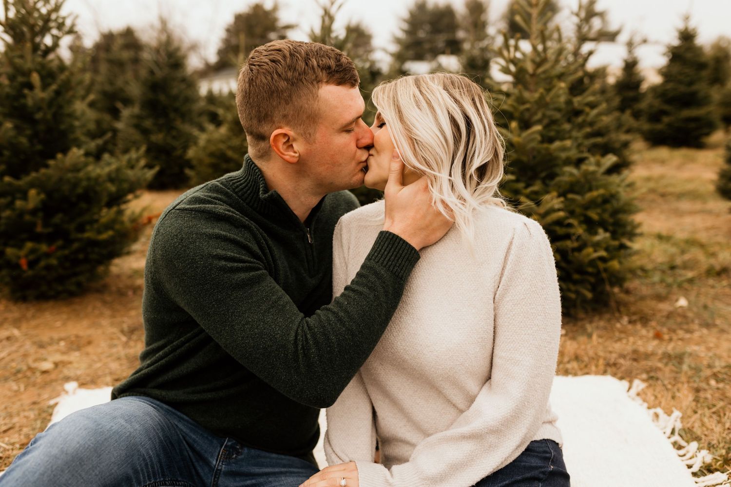 Couple sharing a romantic kiss at a Christmas tree farm.