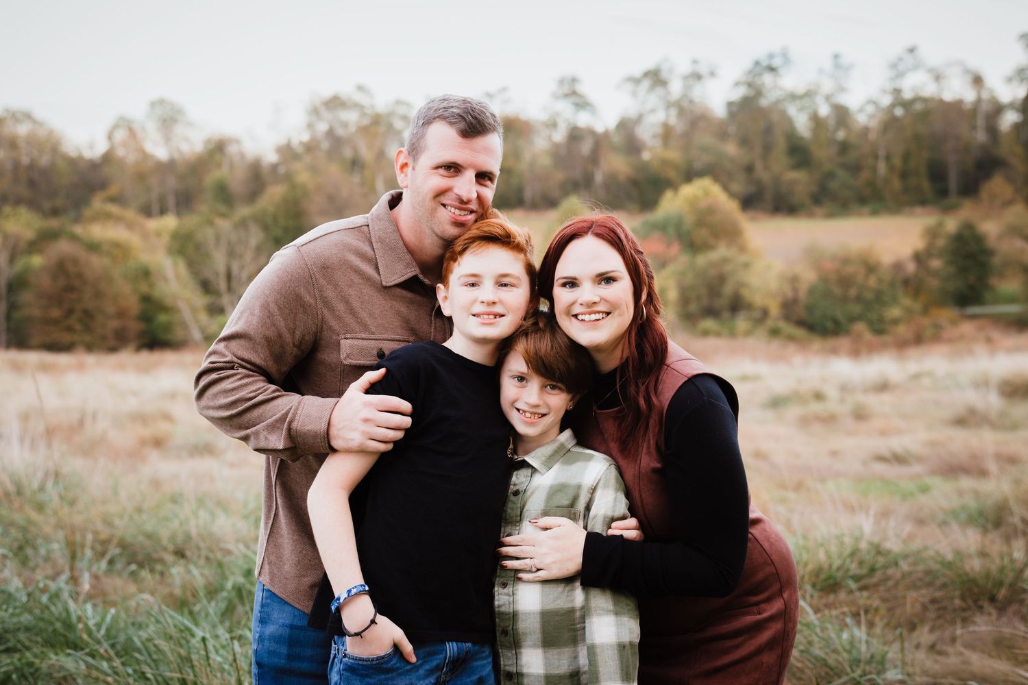 Happy family of four with two redhead boys posing together in an autumn field during outdoor family portrait session.