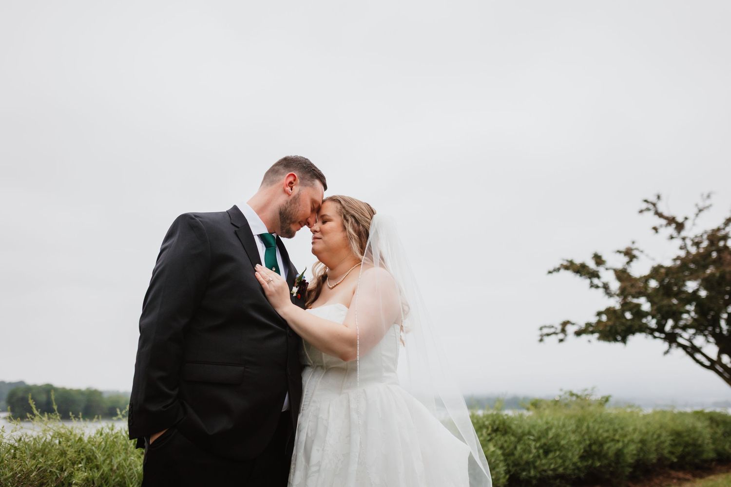 Bride and groom share a tender forehead touch moment outdoors on an overcast wedding day.