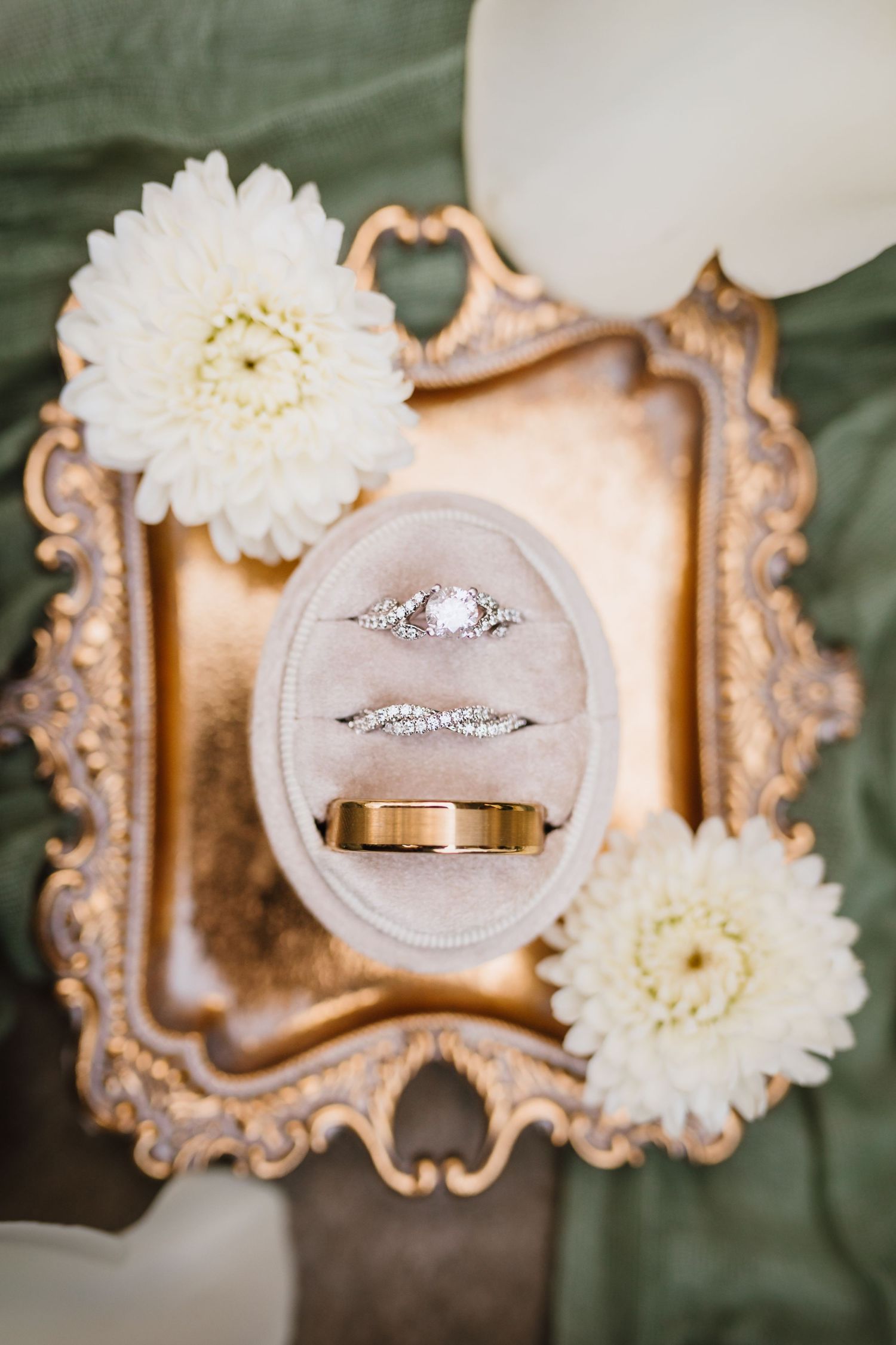 Elegant wedding rings displayed in a velvet oval box on a gold ornate tray with white dahlias.