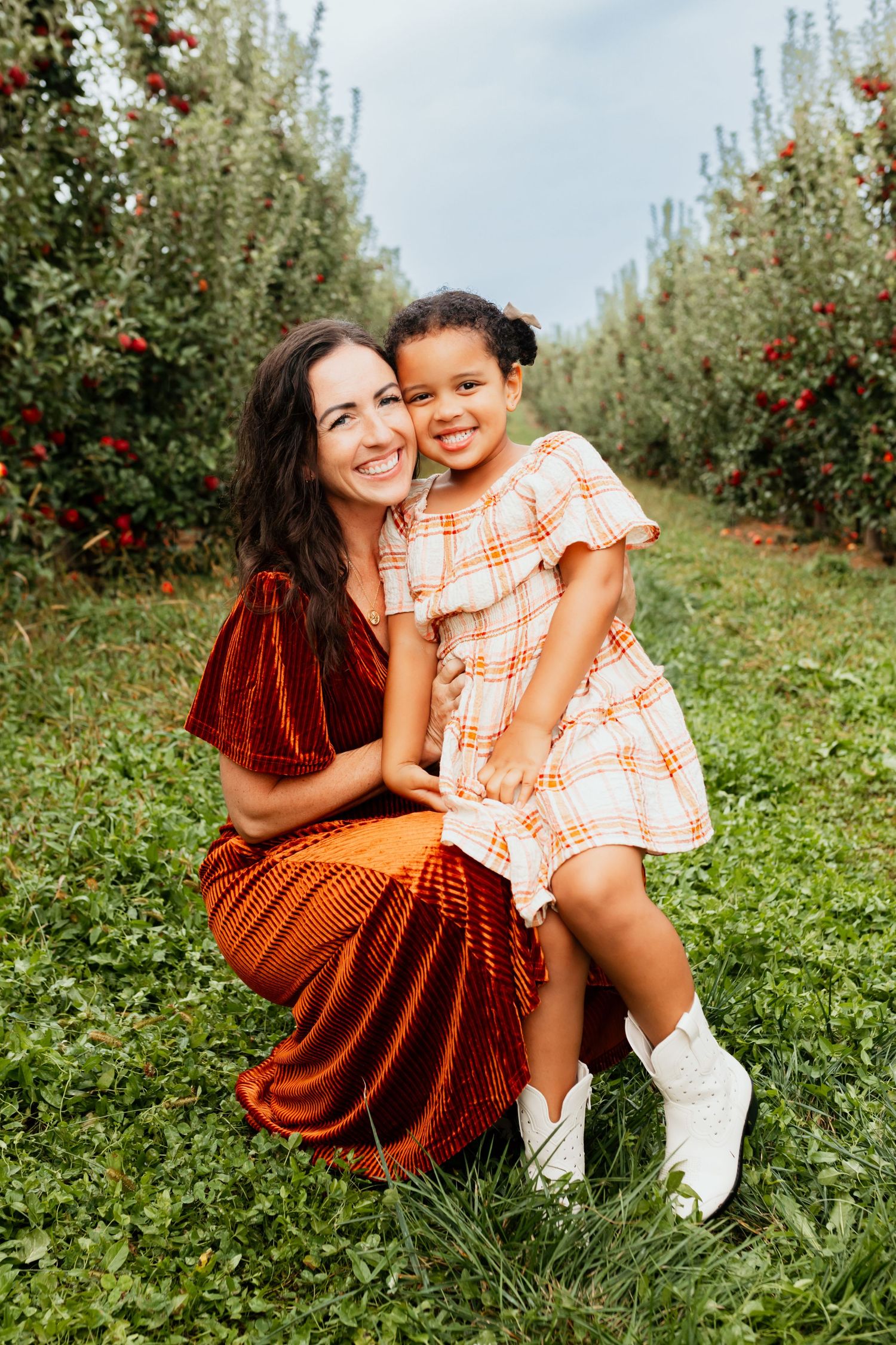 Mother and daughter smiling together in apple orchard in autumn.