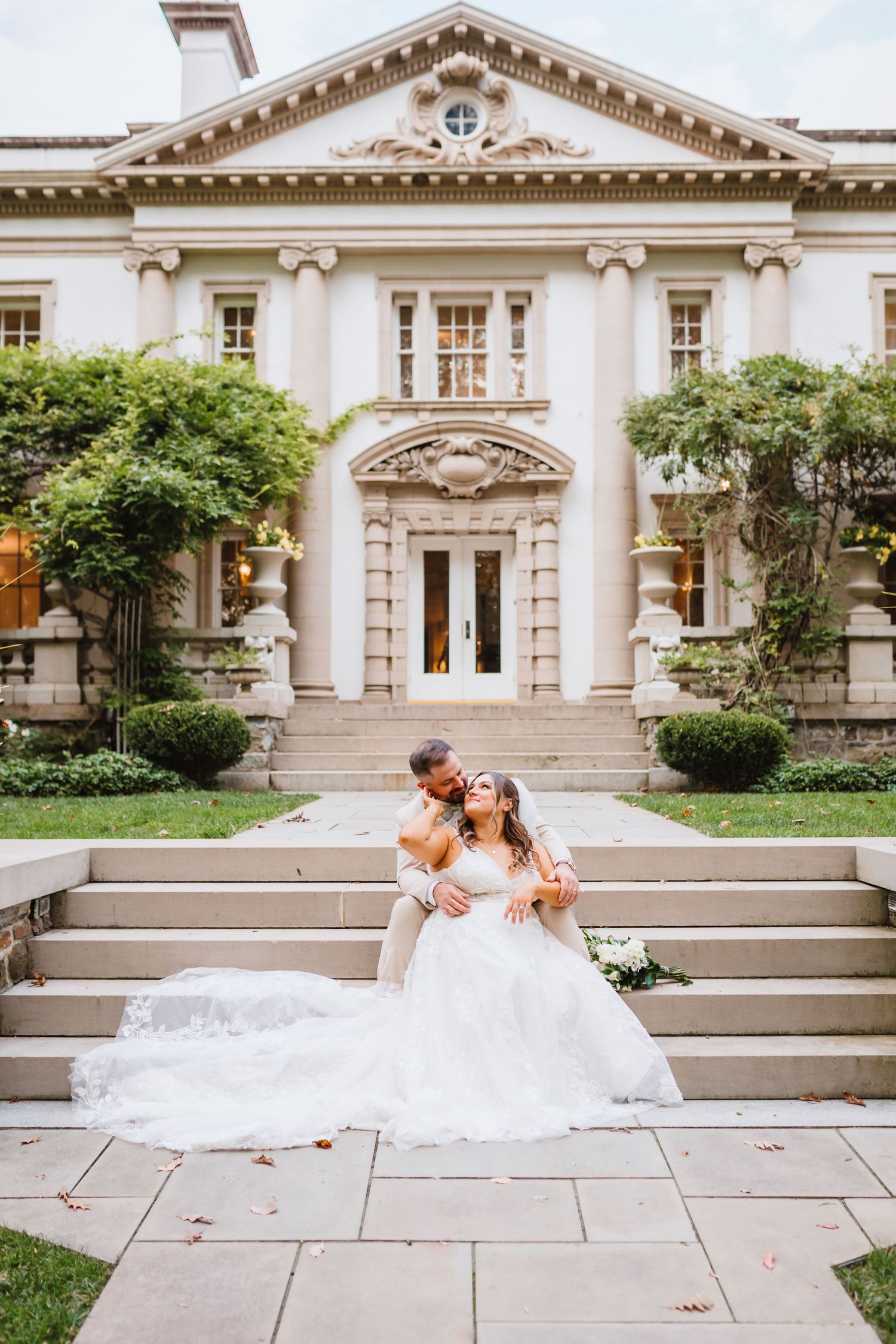 Groom dips bride on stone steps in front of a grand neoclassical mansion wedding venue.