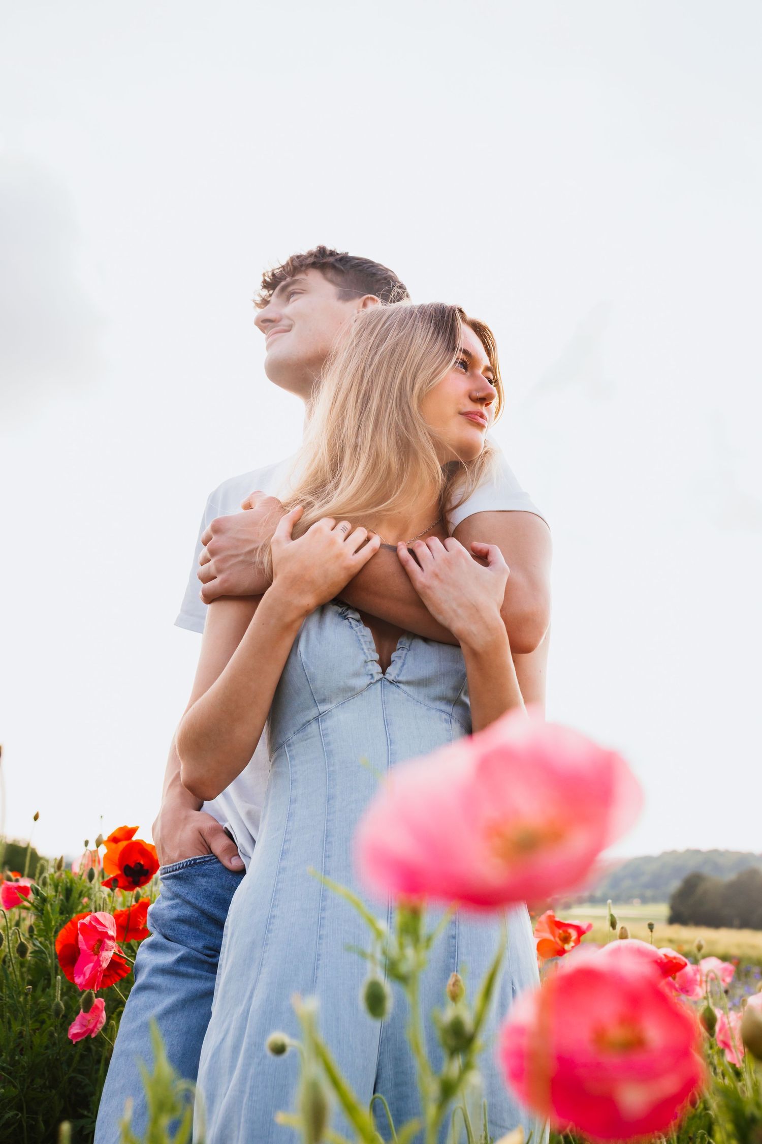 Romantic couple hugging in blooming red poppy field under bright sky.