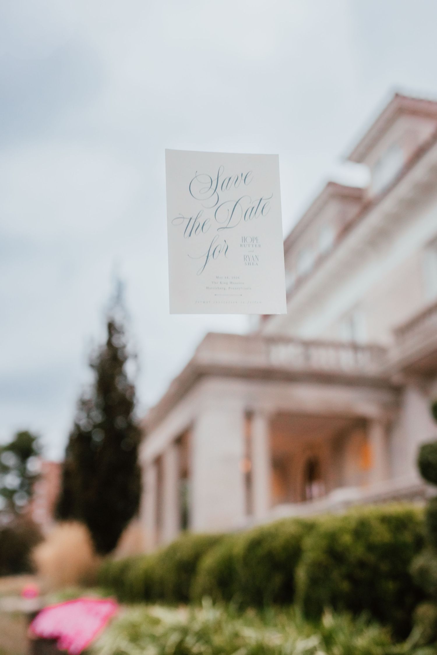 Elegant Save the Date wedding card held up in front of a grand estate venue.
