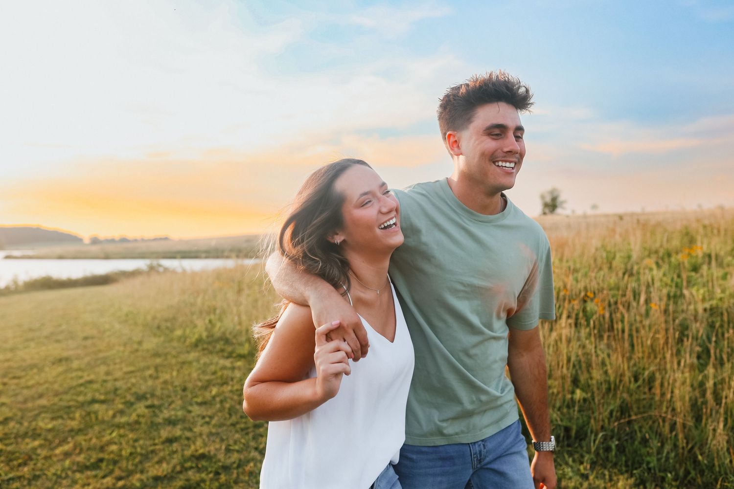 Happy young couple walking together near a field at golden hour sunset.
