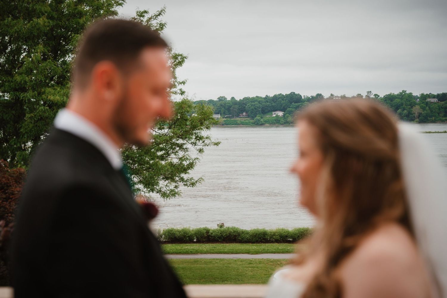Bride and groom share a tender moment outdoors with a serene waterfront backdrop.