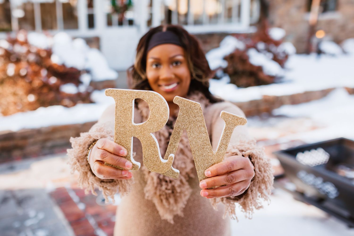 Smiling woman holds glittery gold letters RW in snowy outdoor setting.