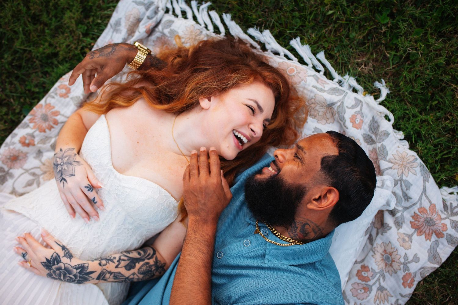 Joyful couple laughing together while lying on a blanket outdoors during an engagement session.