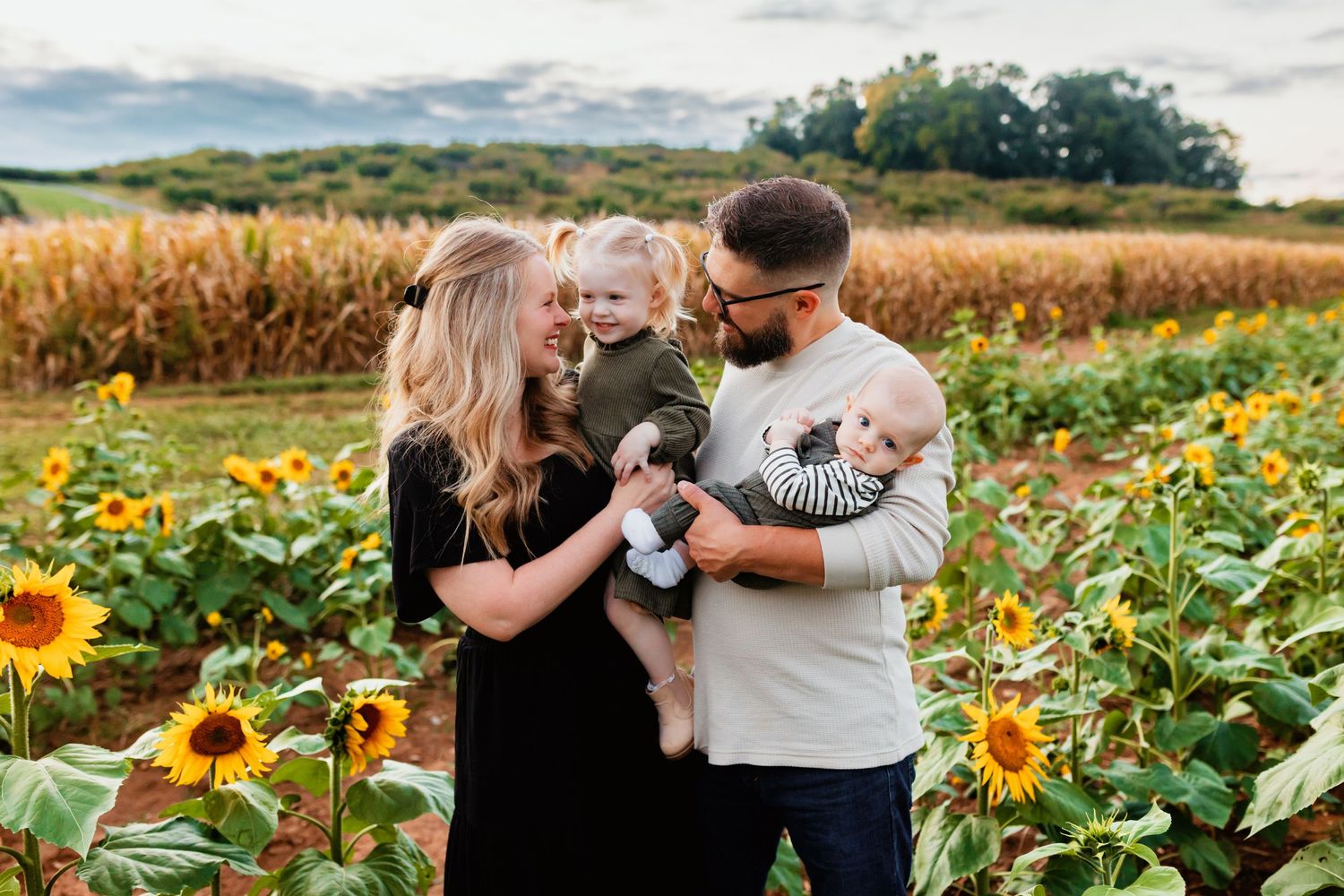 Happy family with two young children posing in sunflower field.